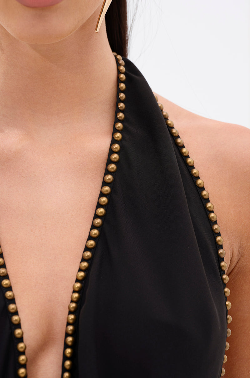 Close-up of a woman wearing the GENIE IN A BOTTLE HALTER TOP—a black chiffon halter with a deep neckline, gold beaded trim, and open-back design that accentuates her neck, shoulders, and flowing dark hair.