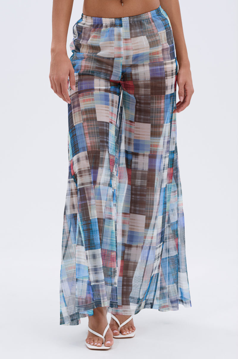 A person models the LIVING THE LIFE PLAID MESH PALAZZO PANT, featuring a flowy, sheer plaid mesh fabric with a wide-leg, high-rise fit, styled with white strappy sandals. The image is cropped from the waist down against a plain background.