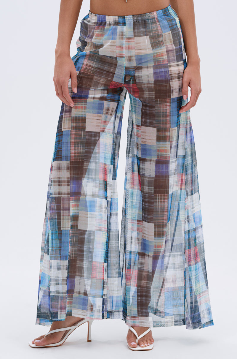 Wearing the LIVING THE LIFE PLAID MESH PALAZZO PANT—sheer, high-rise, wide-leg pants—paired with white heeled sandals, a person stands against a plain background.