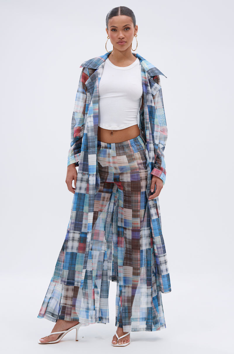 A woman wears the LIVING THE LIFE PLAID MESH PALAZZO PANT, featuring blue, brown, and white checkered mesh over a white cropped top and heels, paired with a sheer long coat as she poses against a plain white background.