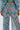 Wearing GRISELDA PRINTED PALAZZO PANTS with a vibrant blue, yellow, pink, green, and white geometric chevron pattern; coordinated top features the same design. Only lower torso and upper legs are shown.