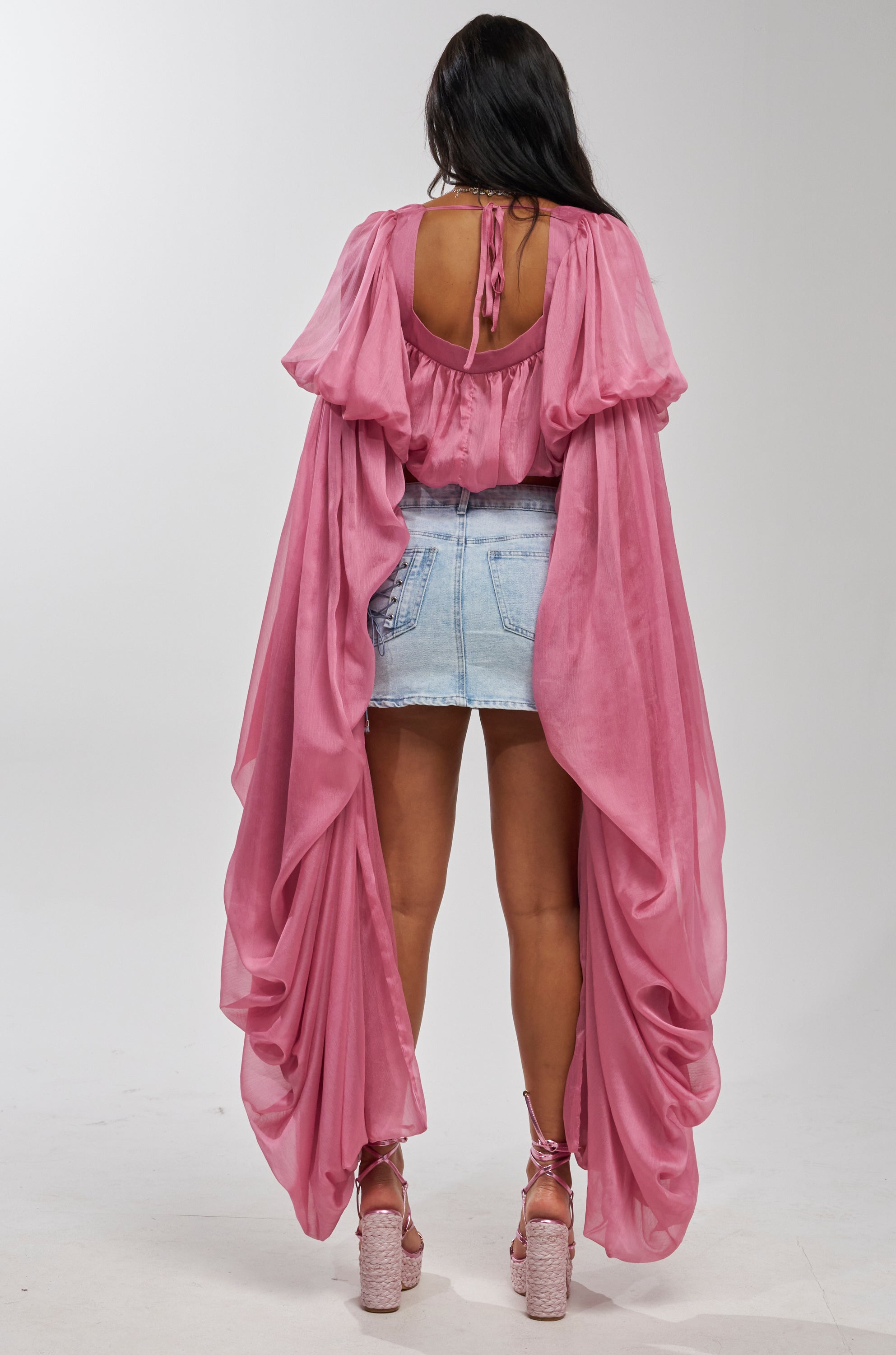 A person faces away, wearing the SLOUCHY SQUARE NECK LONG SLEEVE BLOUSE TOP IN MAUVE with exaggerated sleeves, a light blue denim mini skirt, and pink platform heels against a plain white background.