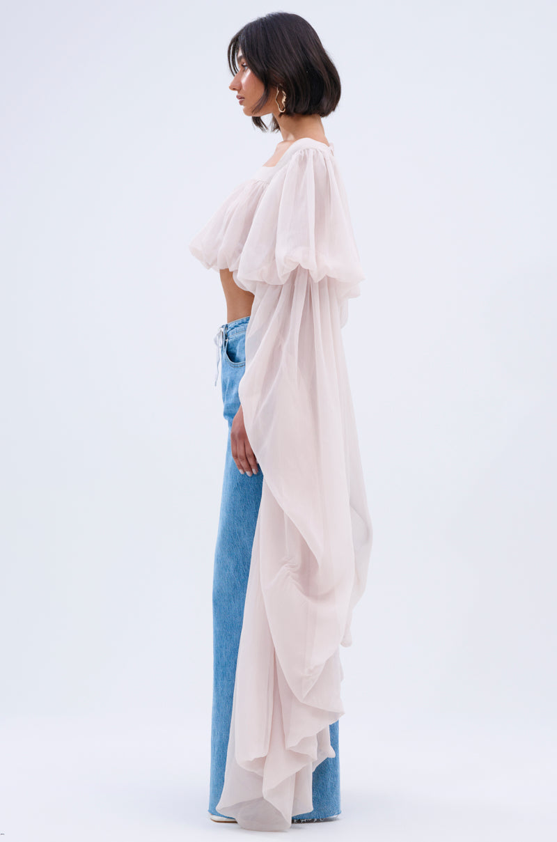 A woman with a dark bob stands in profile, wearing high-waisted blue jeans and the SLOUCHY SQUARE NECK LONG SLEEVE BLOUSE TOP with sheer fabric, billowy sleeves, and a long train against a minimalist background.