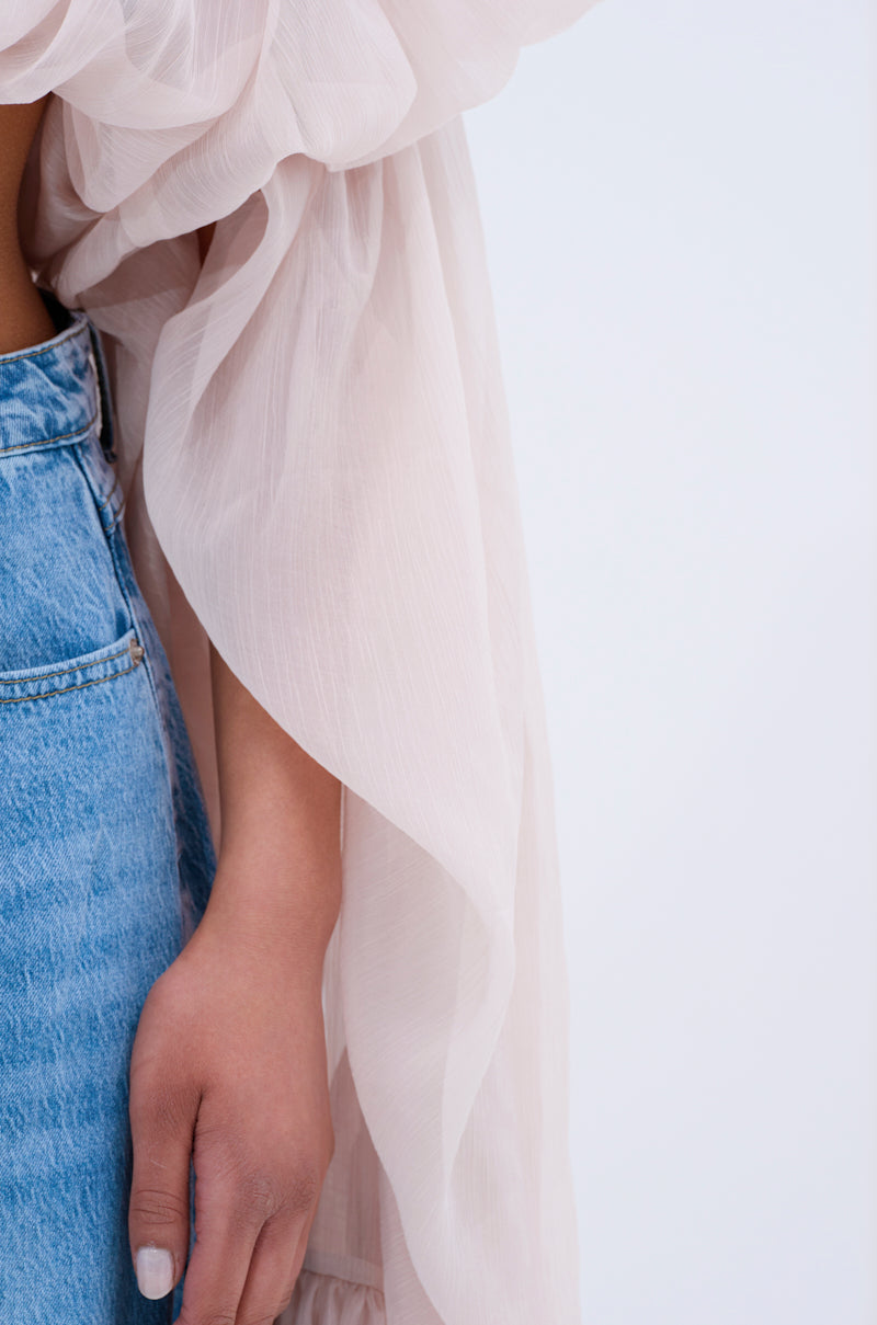 Wearing the SLOUCHY SQUARE NECK LONG SLEEVE BLOUSE TOP in sheer light pink with billowy sleeves and blue denim jeans, a person stands with their arm by their side against a plain light background.