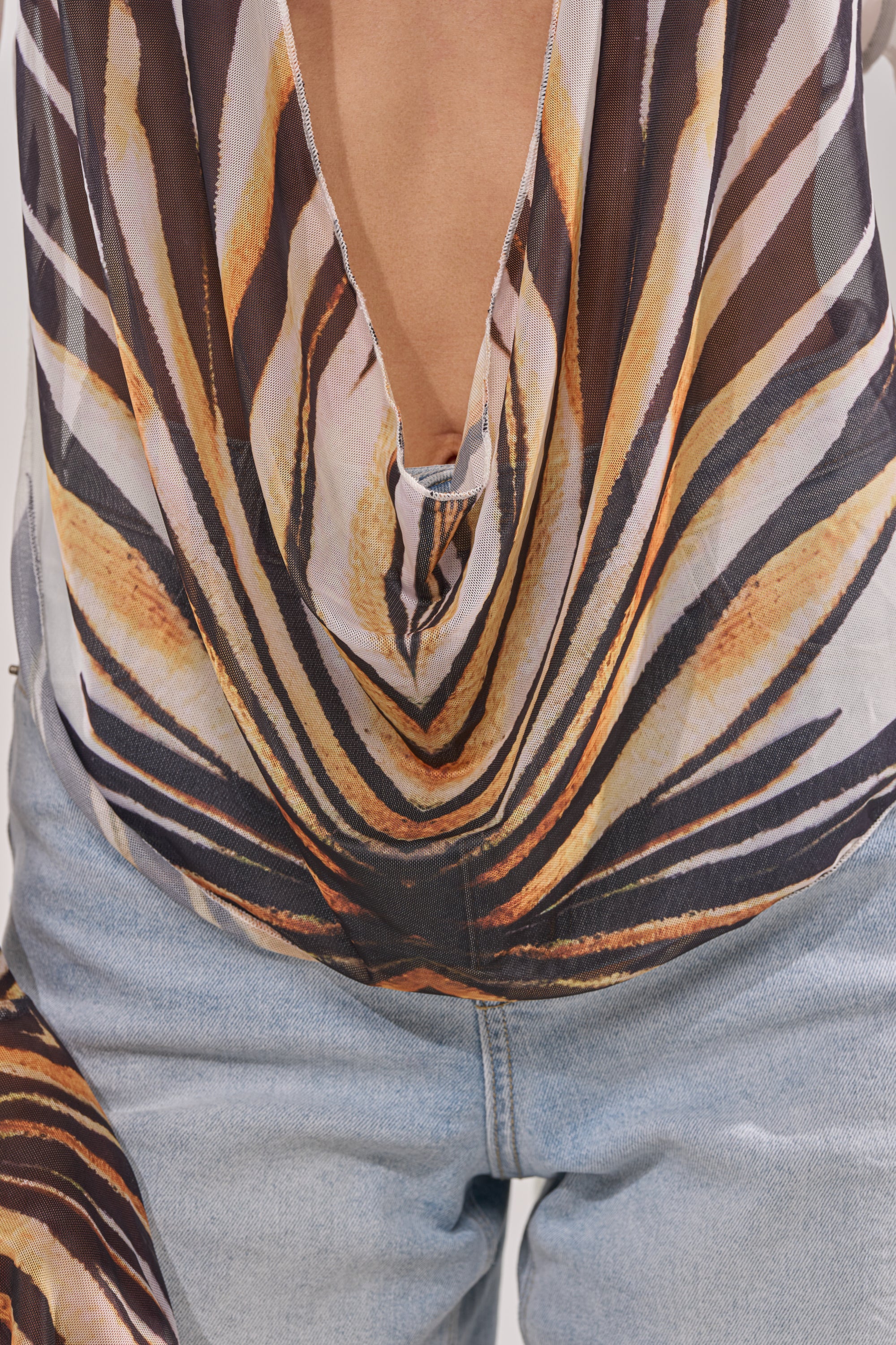 Someone in light blue jeans and the PRIMAL SPIRIT BLOUSE, featuring a low-cut cowl neckline and bold, abstract stripes in orange, yellow, black, and white. 9