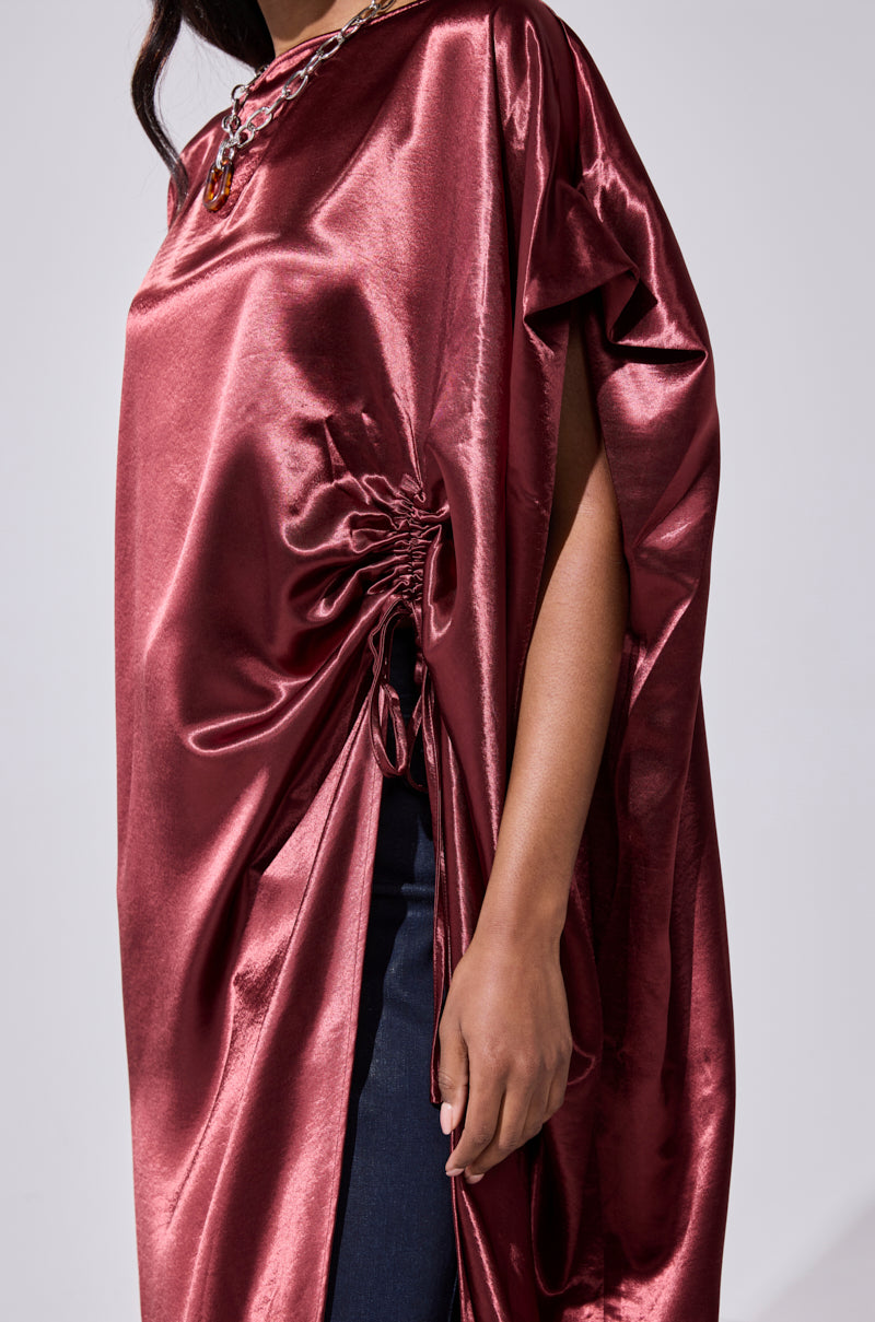 A person models the CLARA SIDE RUCHED BLOUSE in shiny dark red, posing against a neutral background with only the lower half of their face and upper body visible. 7