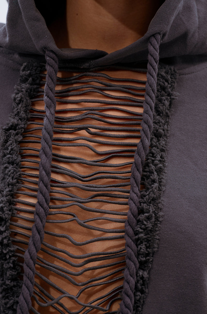 Close-up of the STRESSED AND DISTRESSED SWEATHSIRT, featuring thick drawstrings and horizontal, frayed cutouts on the front panel that reveal skin. The dark gray fabric edges add textured, worn appeal. 7