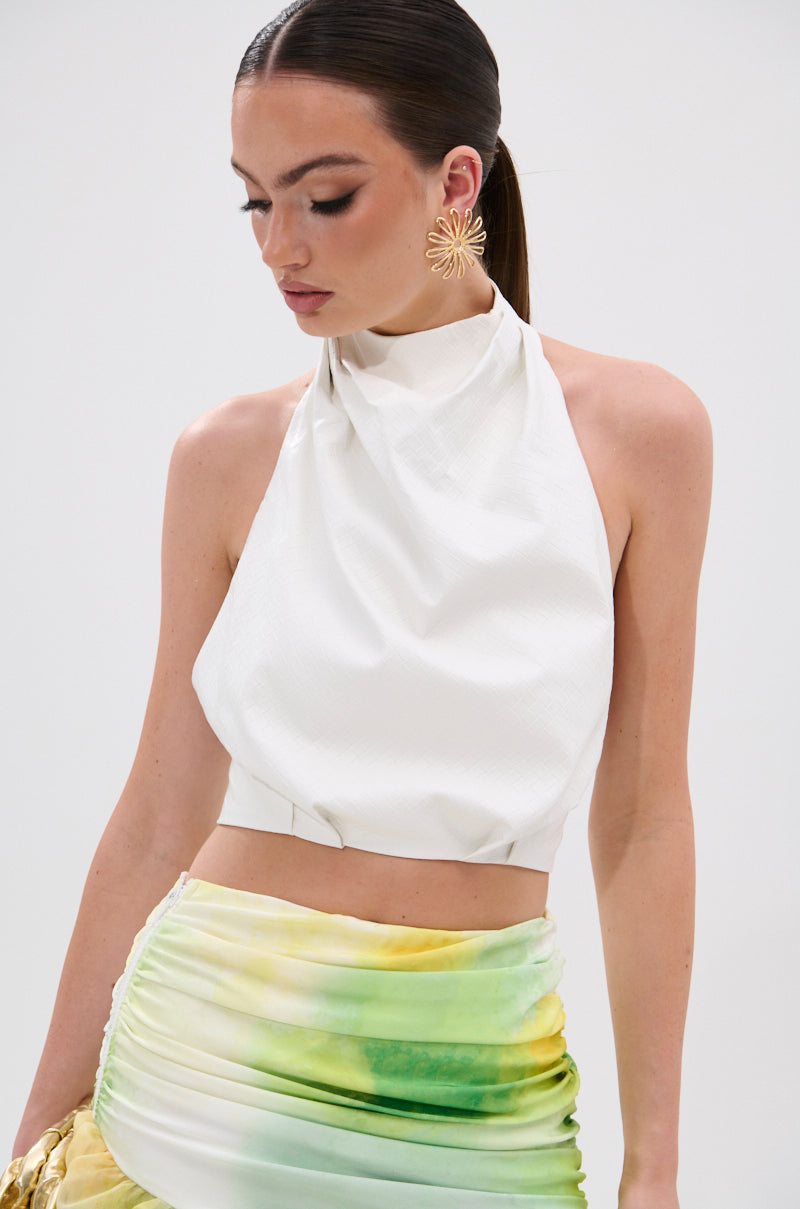 A woman with straight brown hair in a ponytail wears the GOING NO WHERE HALTER BLOUSE and a green-yellow ombre skirt, accessorized with large gold flower earrings, against a plain white background.