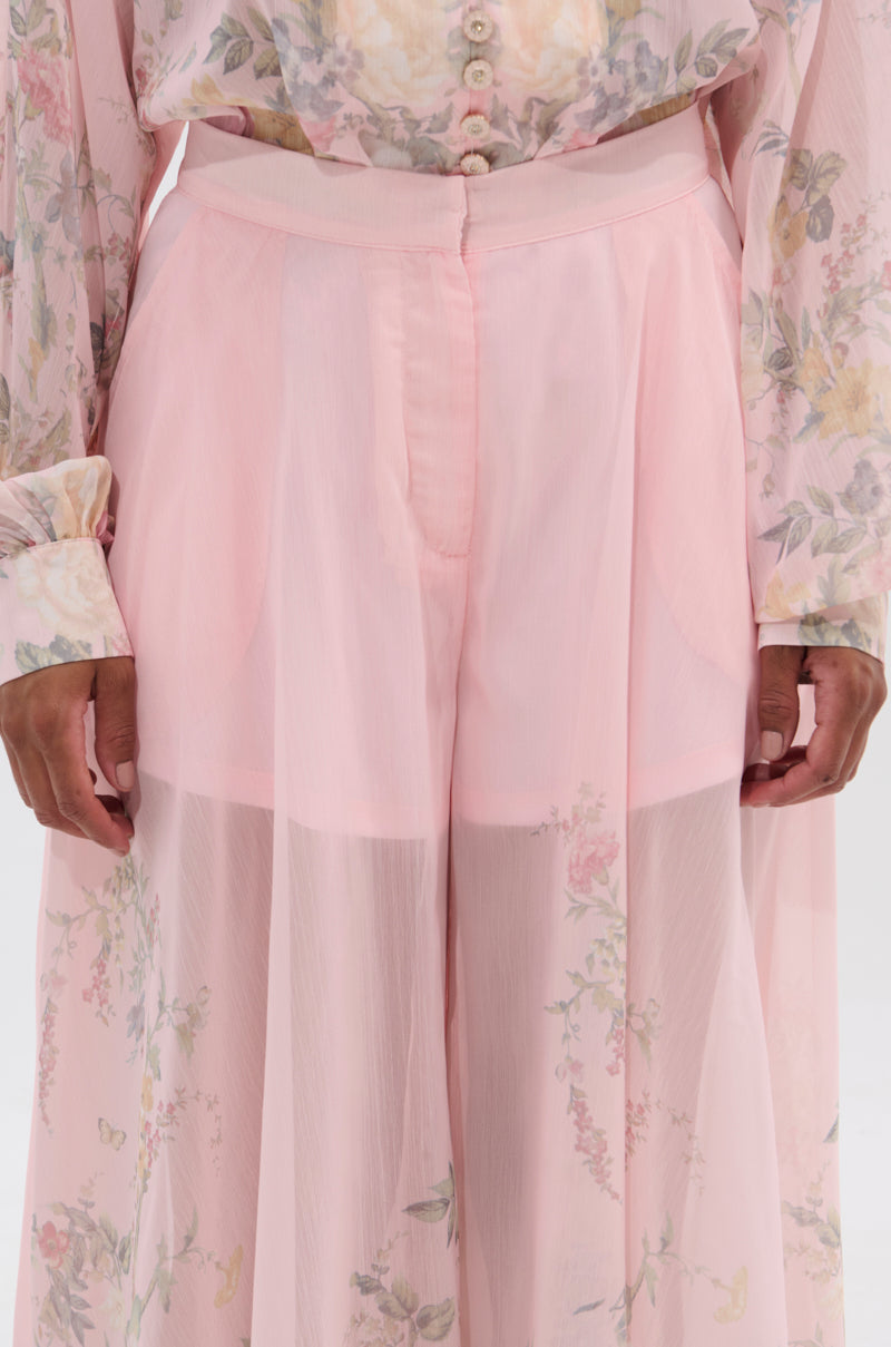 Wearing the SIENNA FLORAL WIDE LEG TROUSER, paired with a light pink sheer long-sleeve top that reveals an inner layer. Only the torso and upper legs are visible. 9