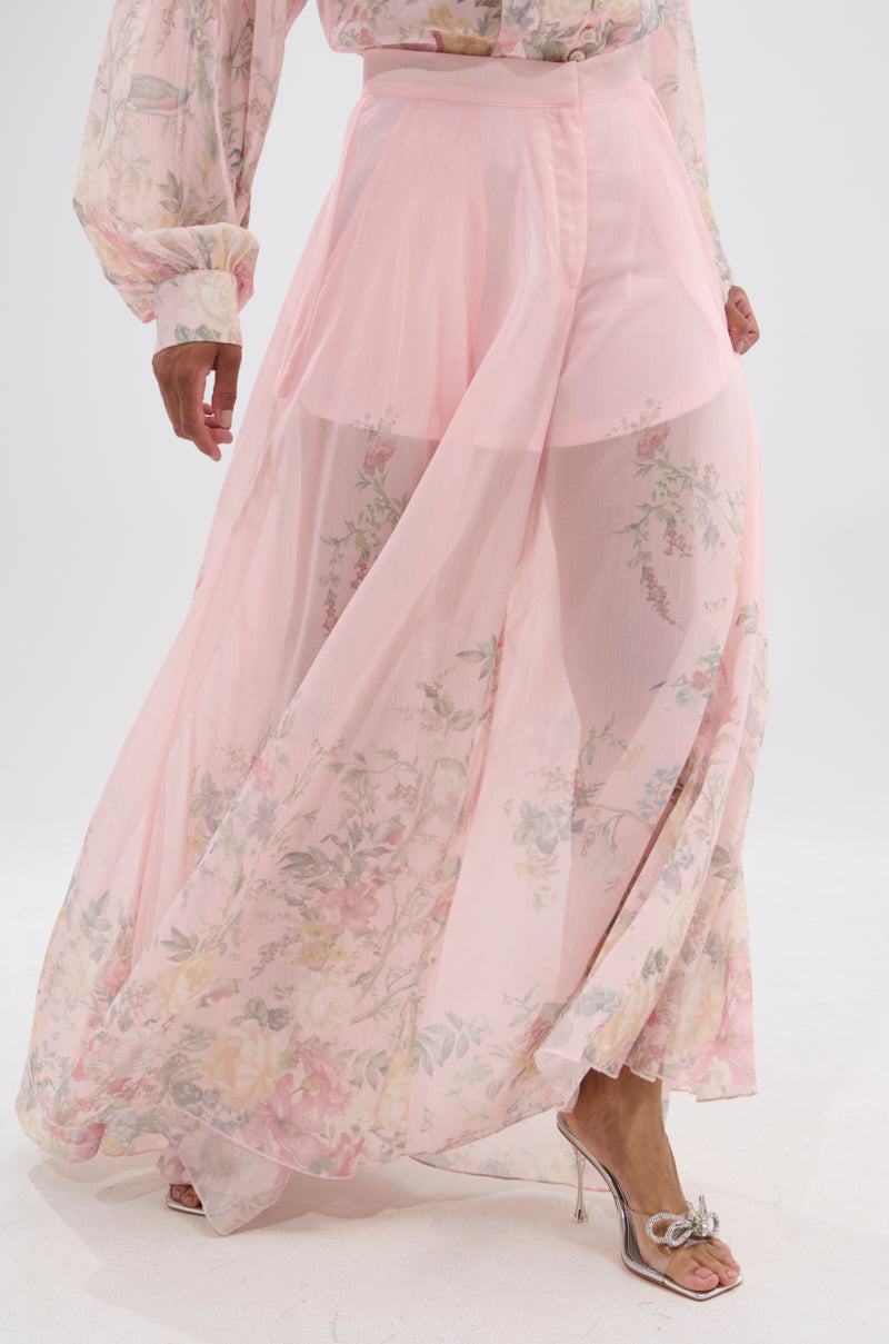 A person models the SIENNA FLORAL WIDE LEG TROUSER with a matching sheer pink blouse and open-toe heeled sandals, posing gracefully against a plain white background. 2