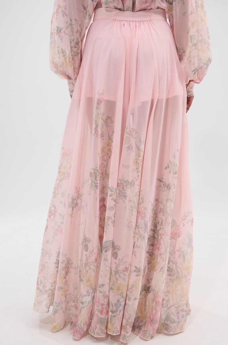 A person wearing the SIENNA FLORAL WIDE LEG TROUSER, featuring a sheer pink chiffon fabric with a floral pattern and visible waistband, stands against a plain white background. 4