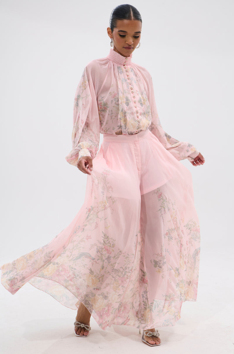 A woman poses gracefully against a white background wearing light pink SIENNA FLORAL WIDE LEG TROUSER and a matching sheer, long-sleeved blouse. 7