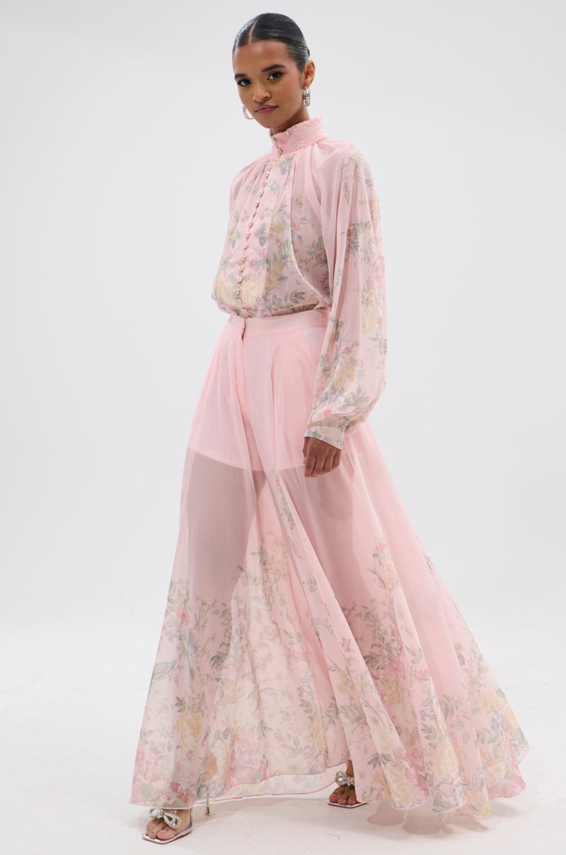 A woman wears the SIENNA FLORAL WIDE LEG TROUSER with a sheer, long-sleeved pastel pink blouse. She stands against a plain white background, facing the camera. 8