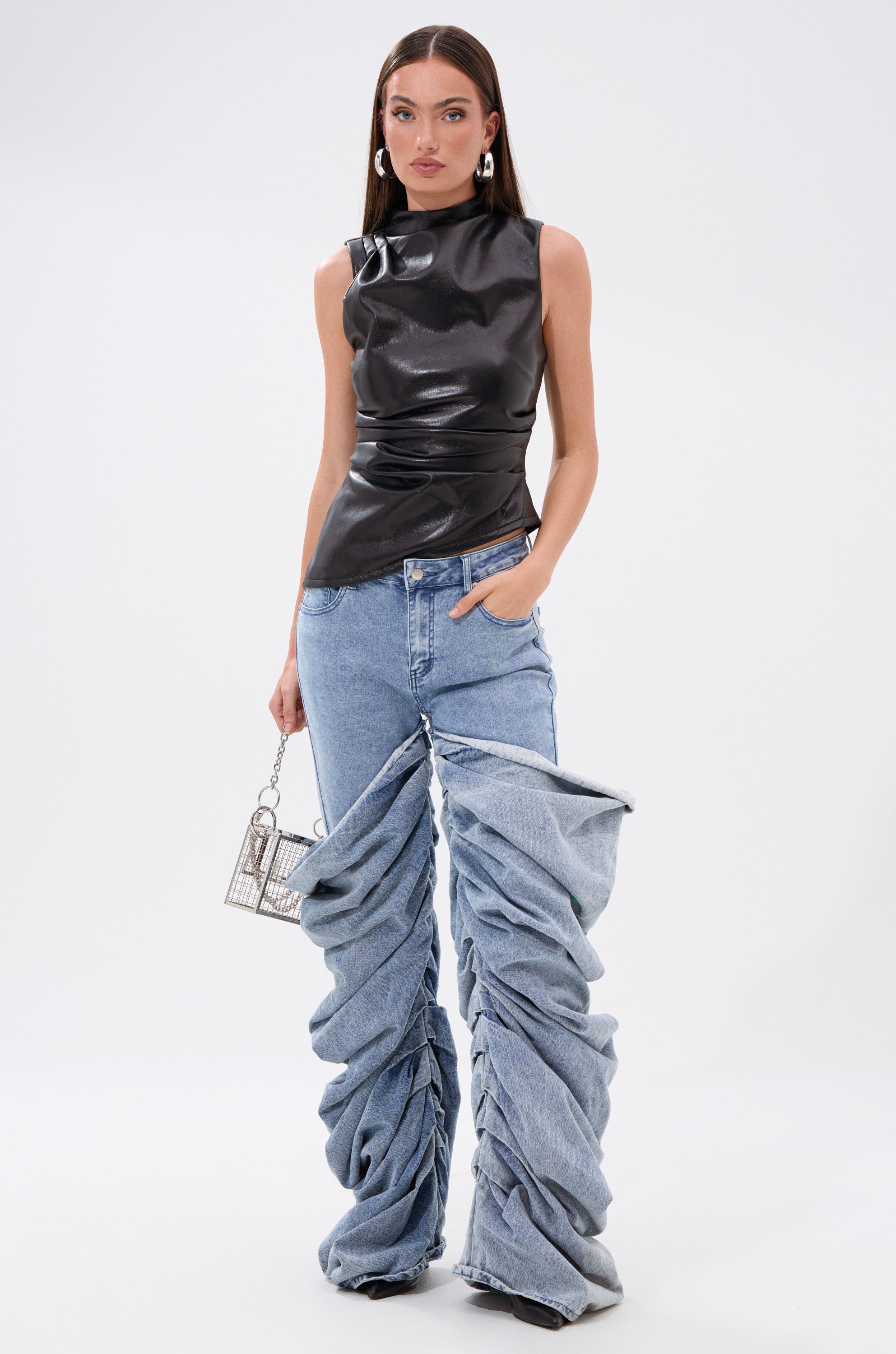 A woman wears the LOCKED AND LOADED FAUX LEATHER BLOUSE—a sleeveless top with an asymmetrical hemline—paired with blue jeans. 4