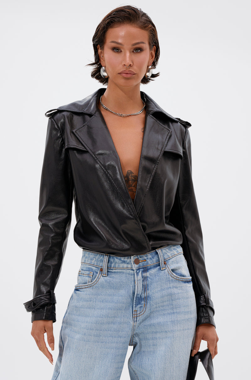 Wearing the TRACIE FAUX LEATHER BLAZER BODYSUIT with light blue jeans and a silver chain necklace, a person stands against a plain white background. 2