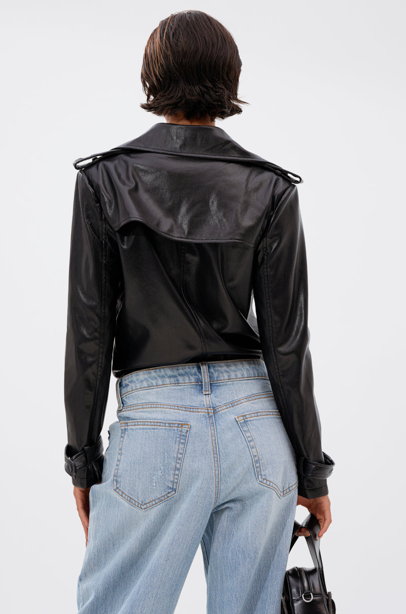 A person with short dark hair is seen from behind, wearing the TRACIE FAUX LEATHER BLAZER BODYSUIT and light blue jeans, holding a small black handbag in their left hand against a plain light background. 4