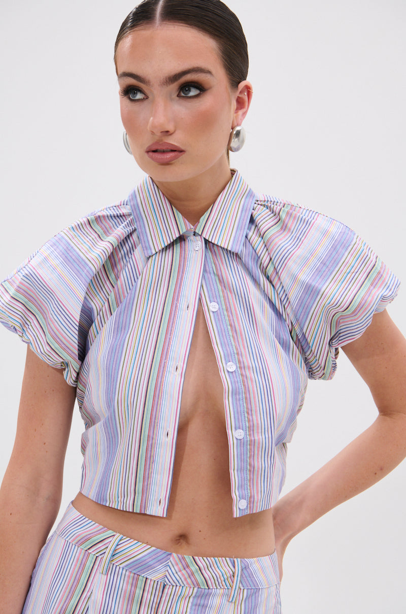 She wears the SUMMER TIME VIBES STRIPE BLOUSE with short sleeves, styled with matching high-waisted pants, slicked-back hair, hoop earrings, and a neutral look for an effortless summer vibe. 0