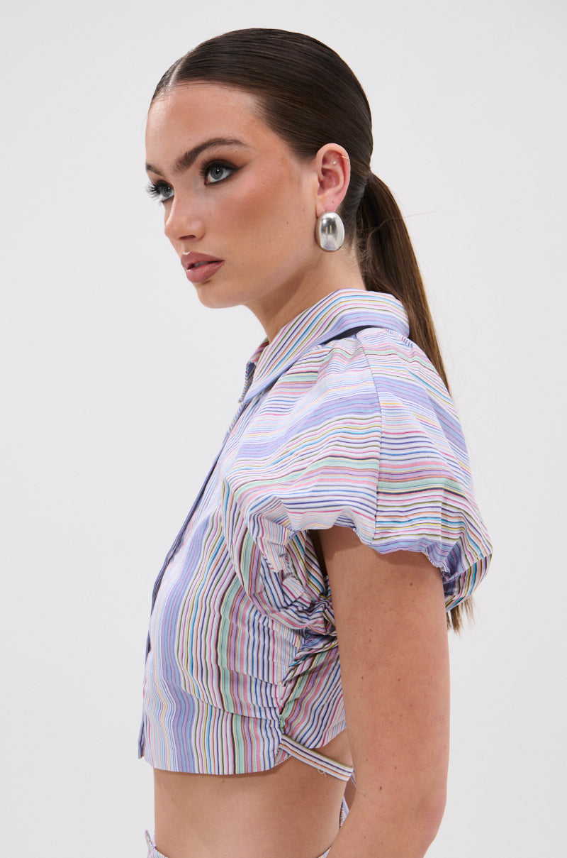 Woman in side profile wears the SUMMER TIME VIBES STRIPE BLOUSE with ruched sides, silver hoop earrings, and a sleek low ponytail, capturing effortless summer vibes against a plain white background. 4