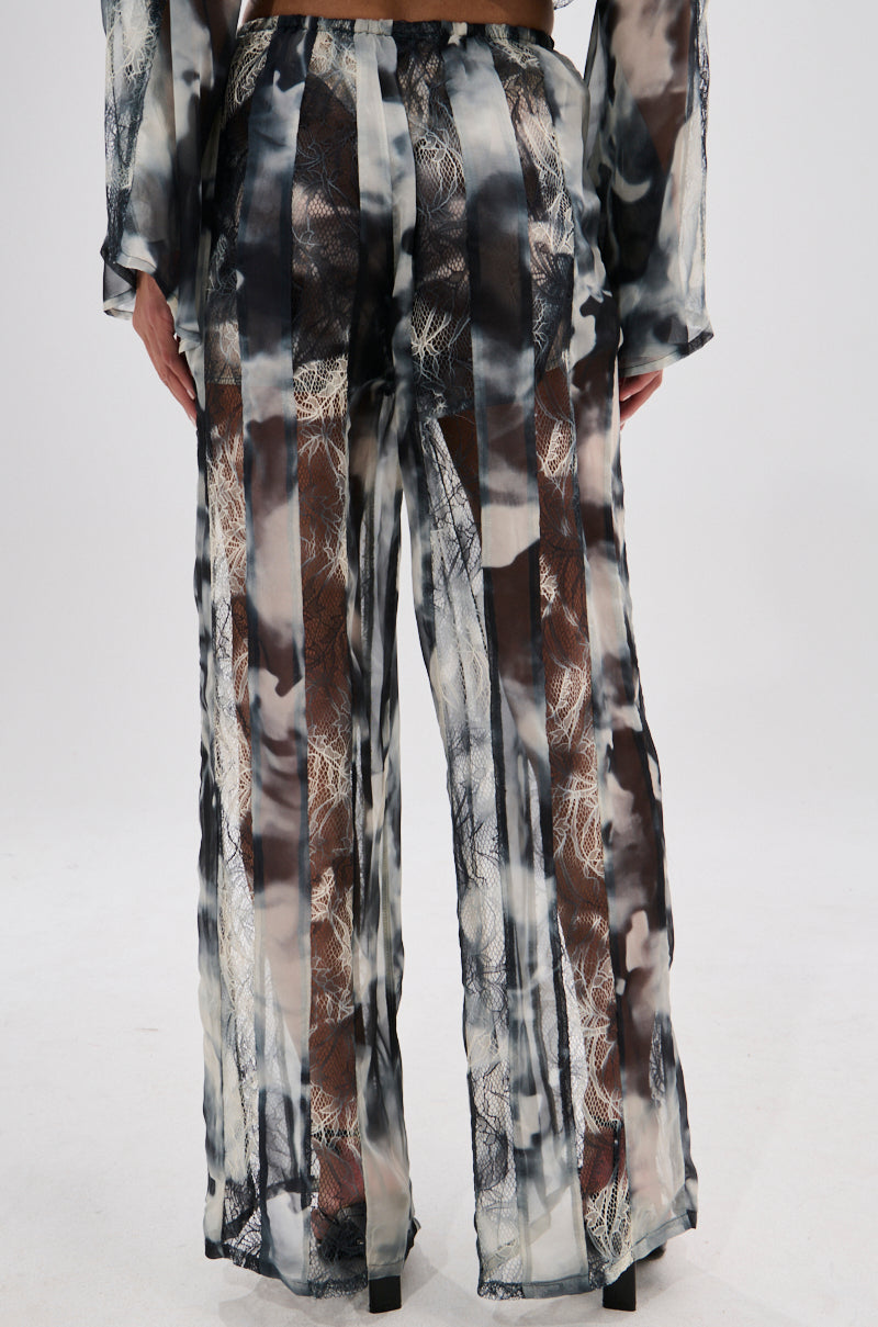 A person wearing the RUBY OMBRE PALAZZO PANT with wide-leg, sheer black-and-white tie-dye fabric and lace detailing. The photo, taken from the back, highlights the flowing silhouette and see-through style. 4