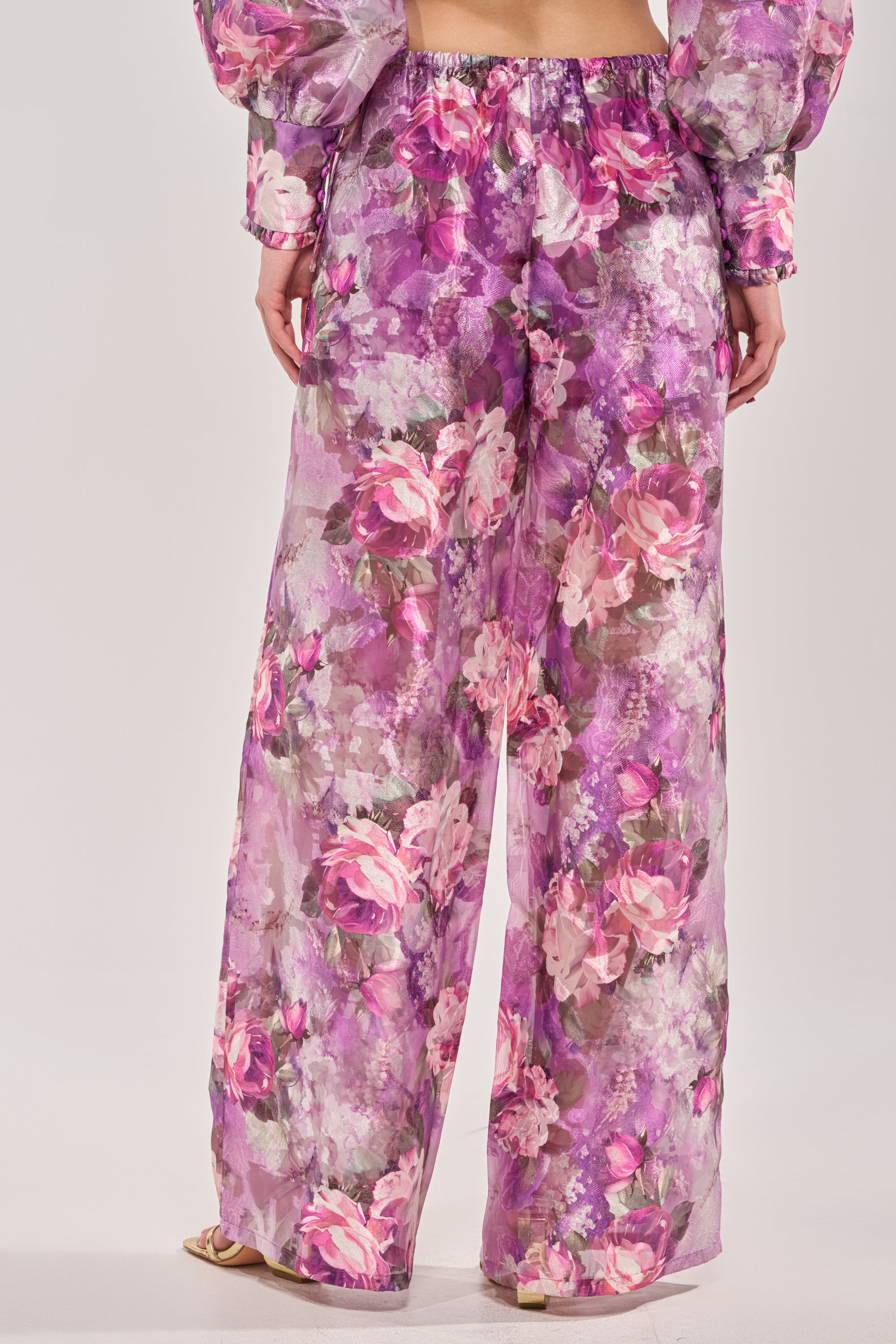 Wearing the KEEP IT FRESH PALAZZO PANT, this look features wide-leg pants with a vibrant pink, purple, and white floral print on sheer fabric, styled with a matching top for chic and stylish resort wear. 3
