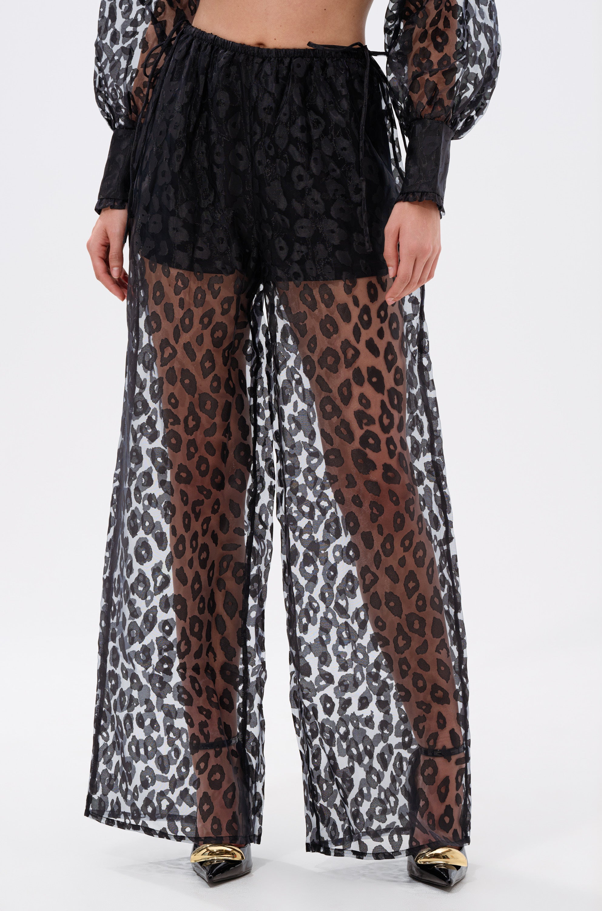 A person wearing the CHEETAH SISTA PALAZZO PANT, featuring black sheer fabric and a bold leopard print.
