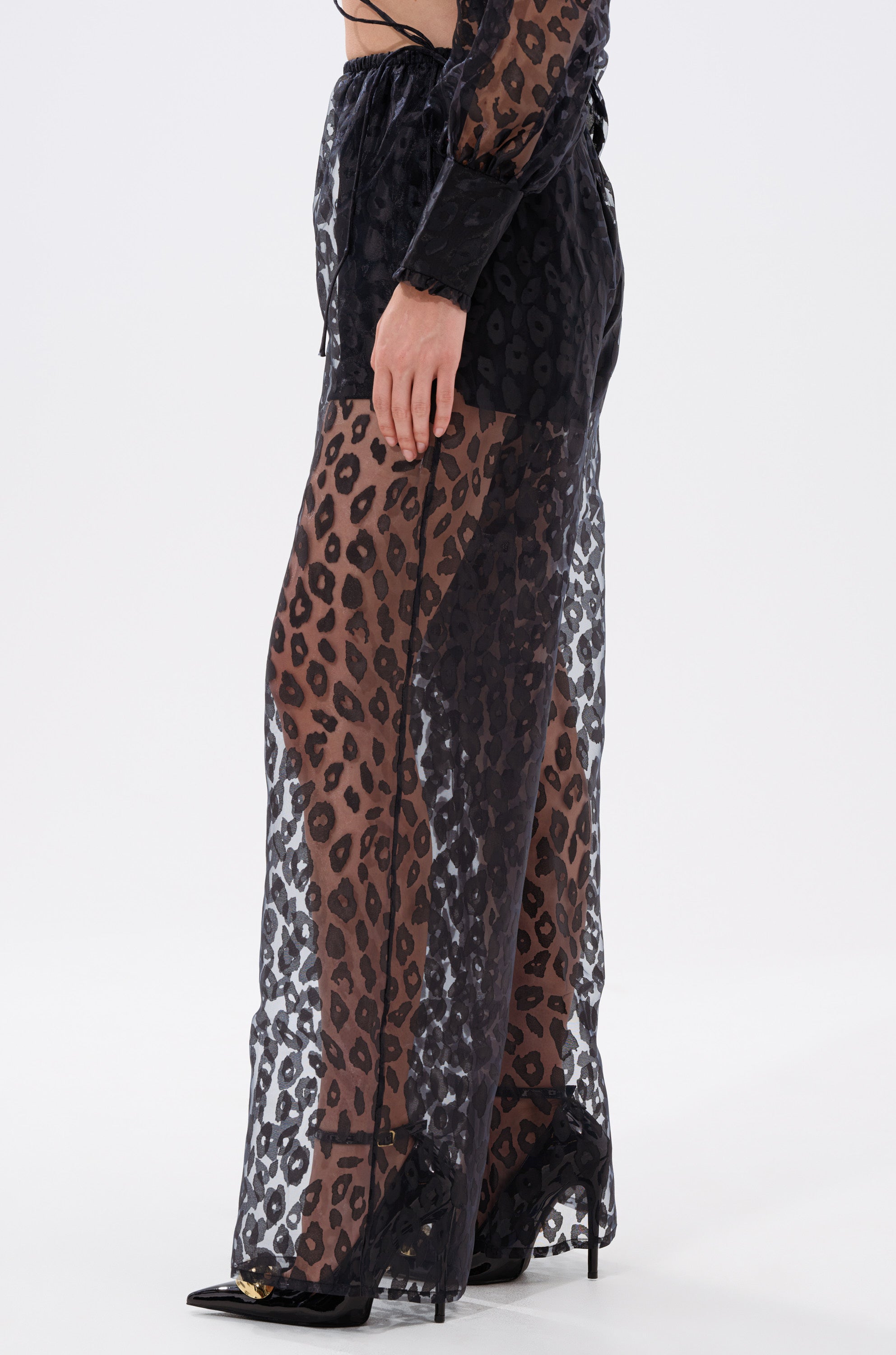 A woman wearing the CHEETAH SISTA PALAZZO PANT, featuring a black and brown leopard print with a high-rise wide-leg silhouette.