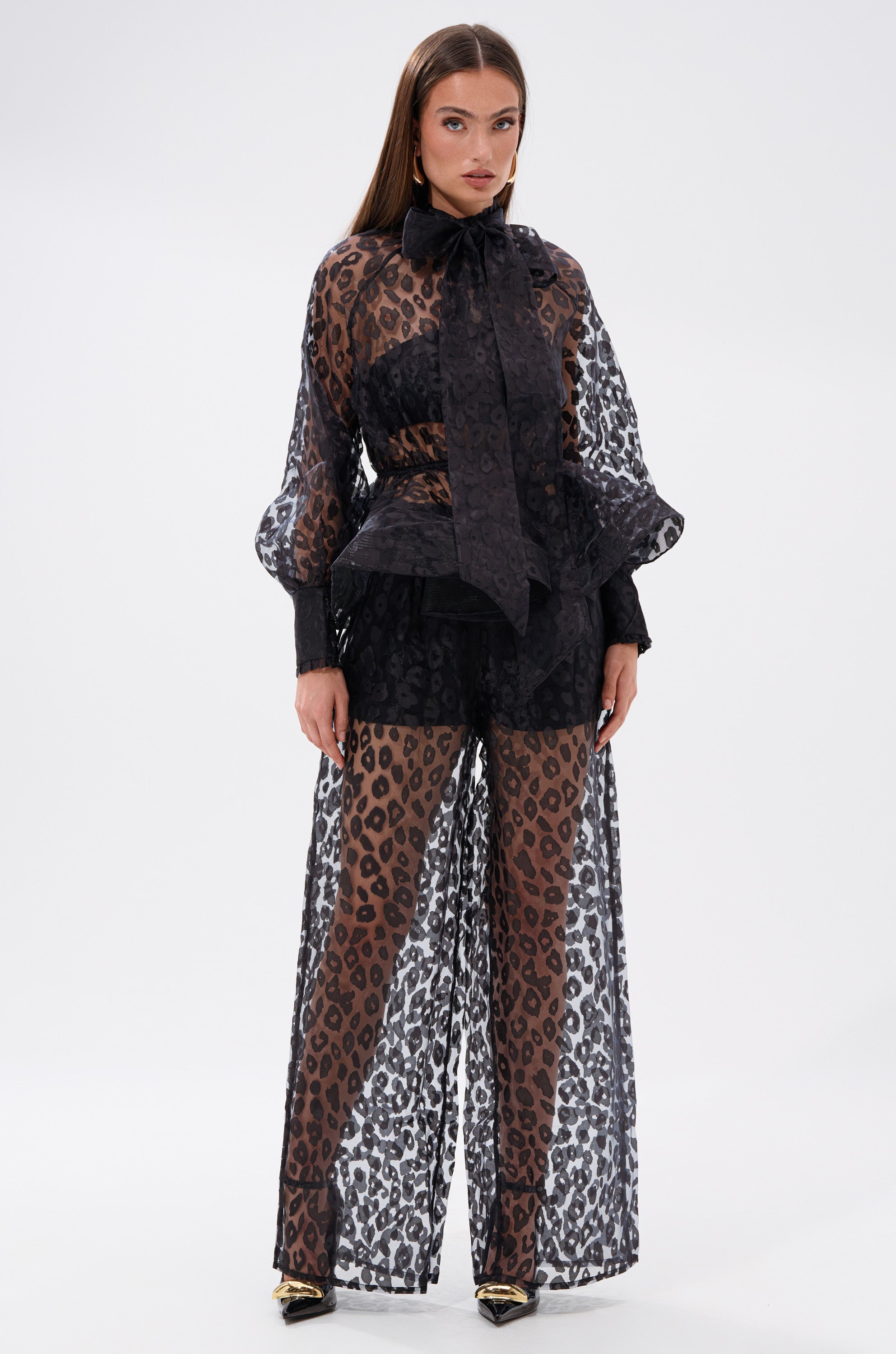A woman showcases effortless style in the CHEETAH SISTA TIE FRONT BLOUSE, her outfit highlighted by its chic peplum silhouette.