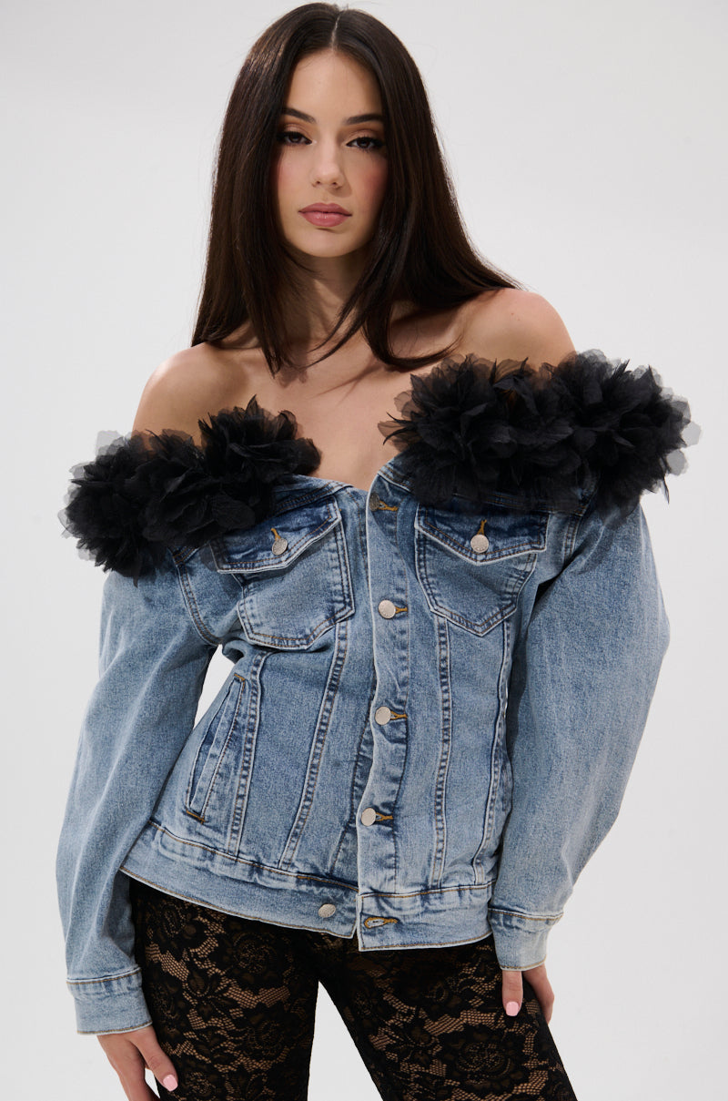 A woman wears the DANA Off The Shoulder Ruffle Detail Denim Top with dramatic black floral tulle accents at the neckline and black lace pants, standing against a plain light background.