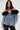 A woman wears the DANA Off The Shoulder Ruffle Detail Denim Top with dramatic black floral tulle accents at the neckline and black lace pants, standing against a plain light background.
