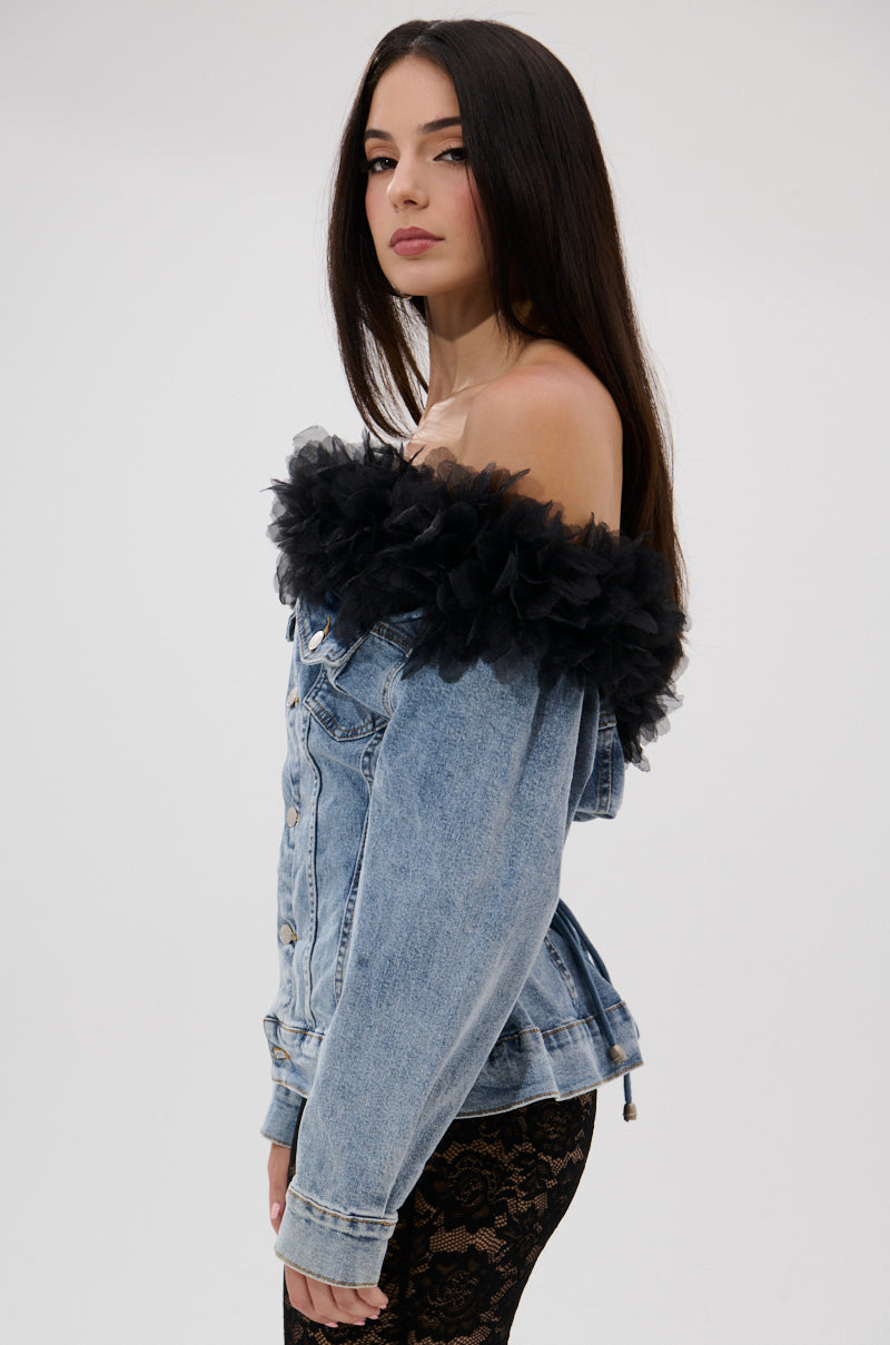 Woman with long dark hair wears the DANA OFF THE SHOULDER RUFFLE DETAIL DENIM TOP, featuring black tulle trim and a lace-up back, paired with black lace pants, standing sideways against a plain light background.