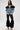A woman poses against a white background in the DANA OFF THE SHOULDER RUFFLE DETAIL DENIM TOP, paired with black lace tiered flared pants and high-heeled sandals. The outfit features ruffled accents and a chic lace-up back.
