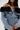 A woman wears the DANA OFF THE SHOULDER RUFFLE DETAIL DENIM TOP with floral tulle ruffle along the neckline, her straight brown hair partly covering her face.