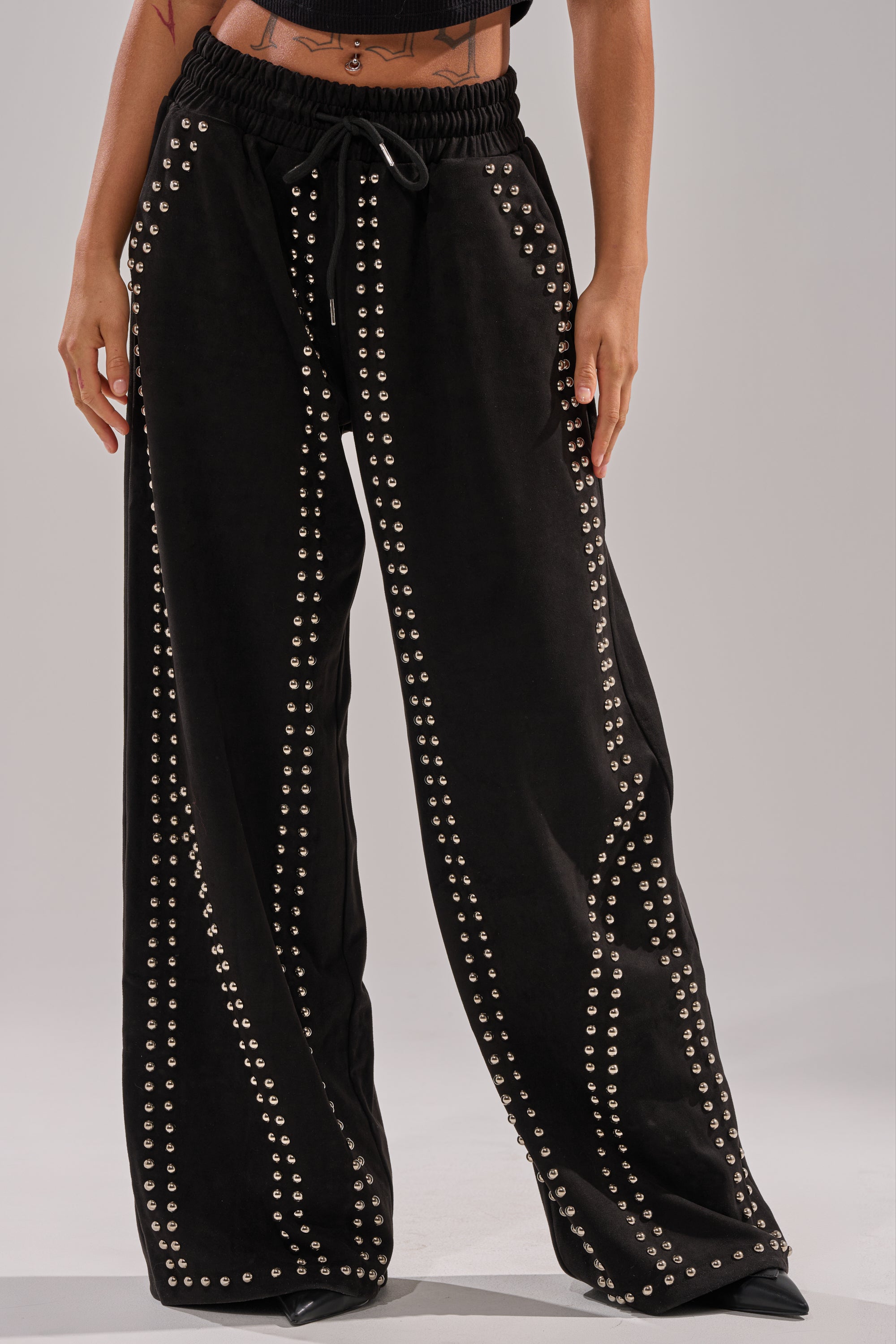 Only the lower torso and legs are visible, wearing the ASHLEY STUDDED WIDE LEG JOGGER adorned with vertical silver studs, paired with a black crop top.