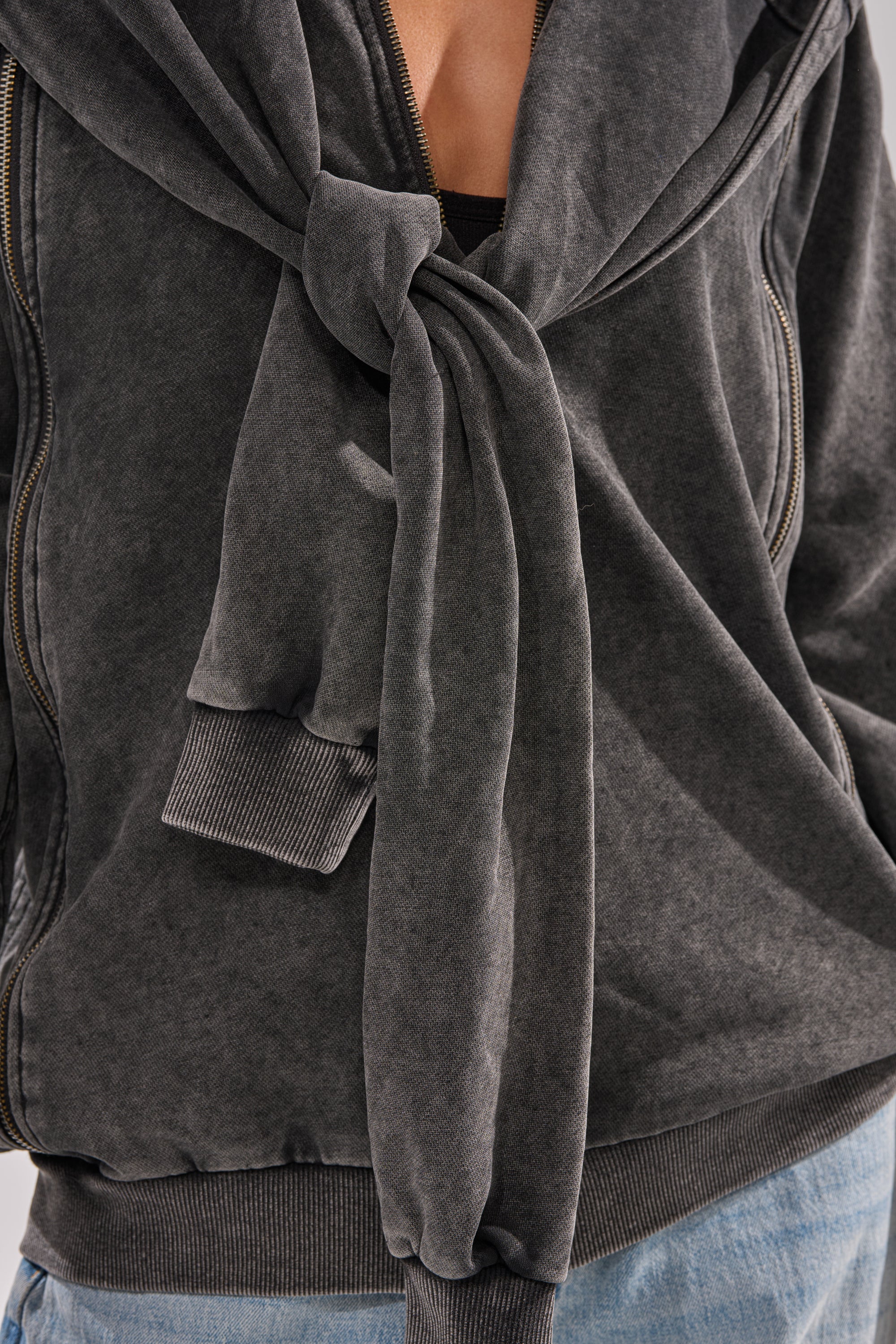 Model wears the COOL GAL TIE SWEATSHIRT in charcoal, styled with the sleeves knotted across the chest and paired with light blue jeans. Focus on upper body and loungewear details.