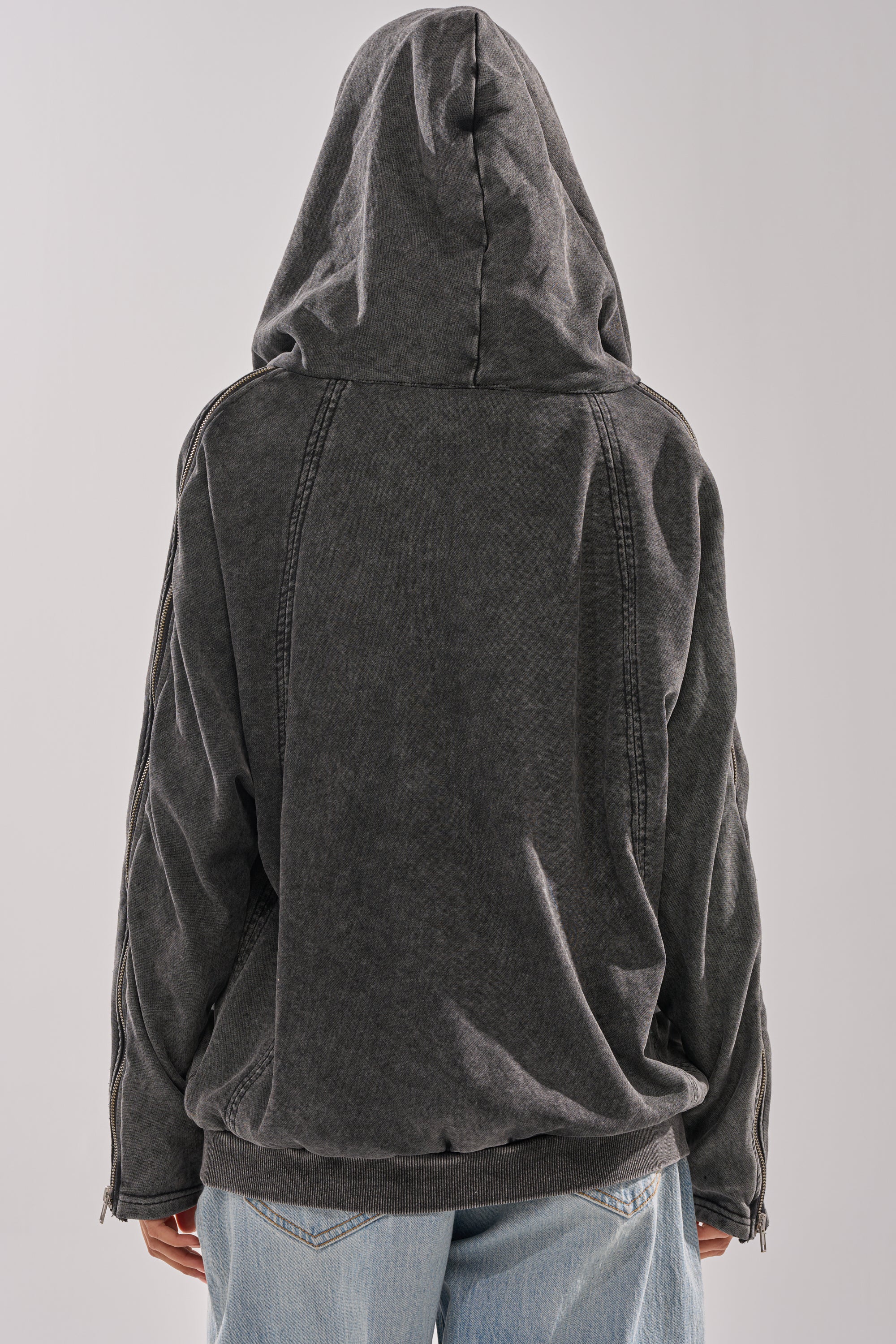 Someone is shown from the back, wearing the COOL GAL TIE SWEATSHIRT with the hood up and paired with light blue jeans, against a plain light background.