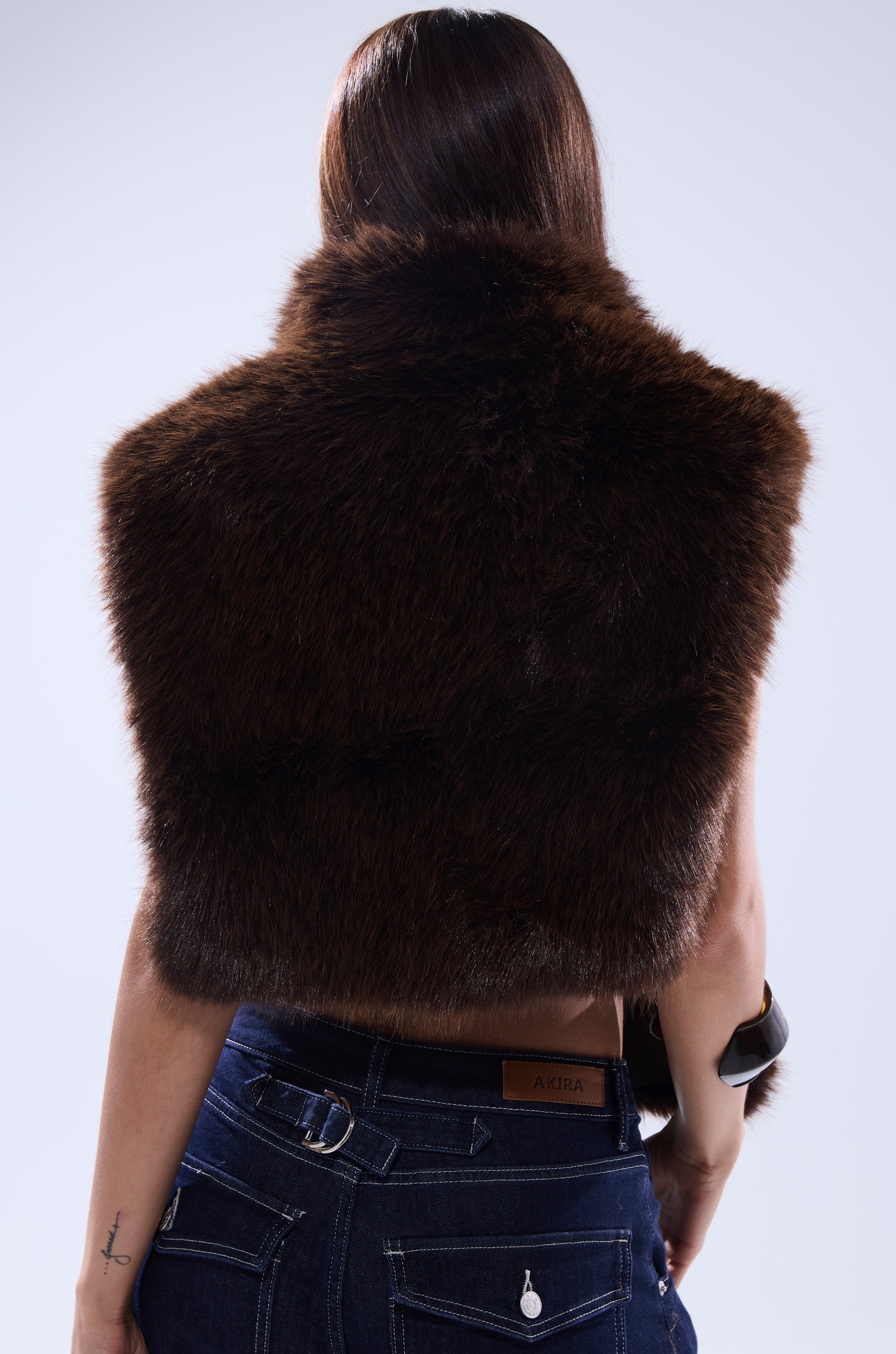 A person with long brown hair, seen from behind, wears the SURE THANG FUR TURTLENECK PULLOVER and dark blue jeans featuring a leather patch labeled "AKIRA," set against a light, plain background. 5