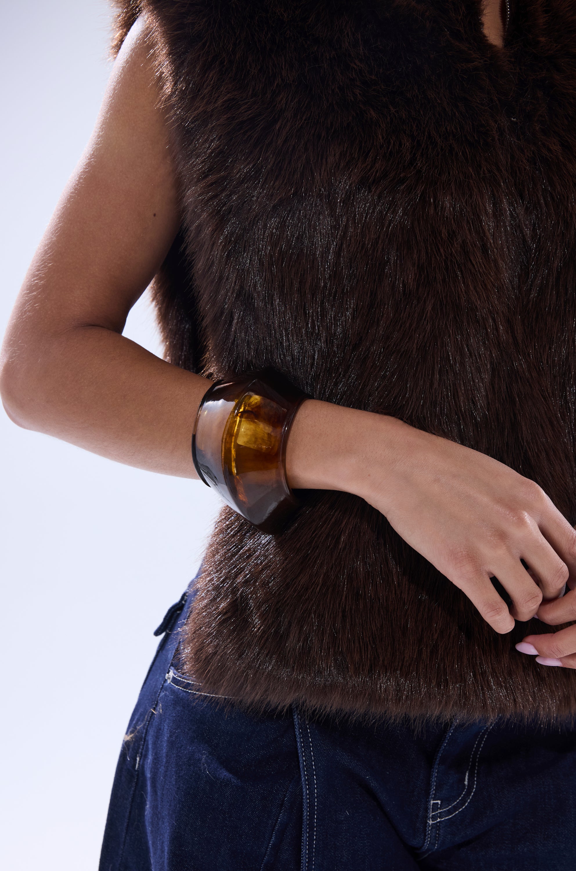 A person wearing the SURE THANG FUR TURTLENECK PULLOVER in chocolate brown, paired with blue jeans and a chunky amber-toned bracelet, rests their hand by their hip against a plain light background. 8