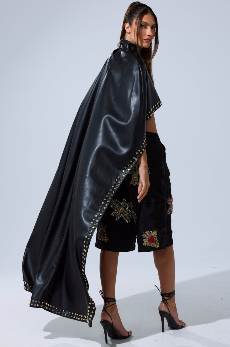 A woman stands in the ALL ABOUT THE DROP TURTLENECK HIGH-LOW BLOUSE, styled with black shorts and high heels, glancing over her shoulder against a plain background.