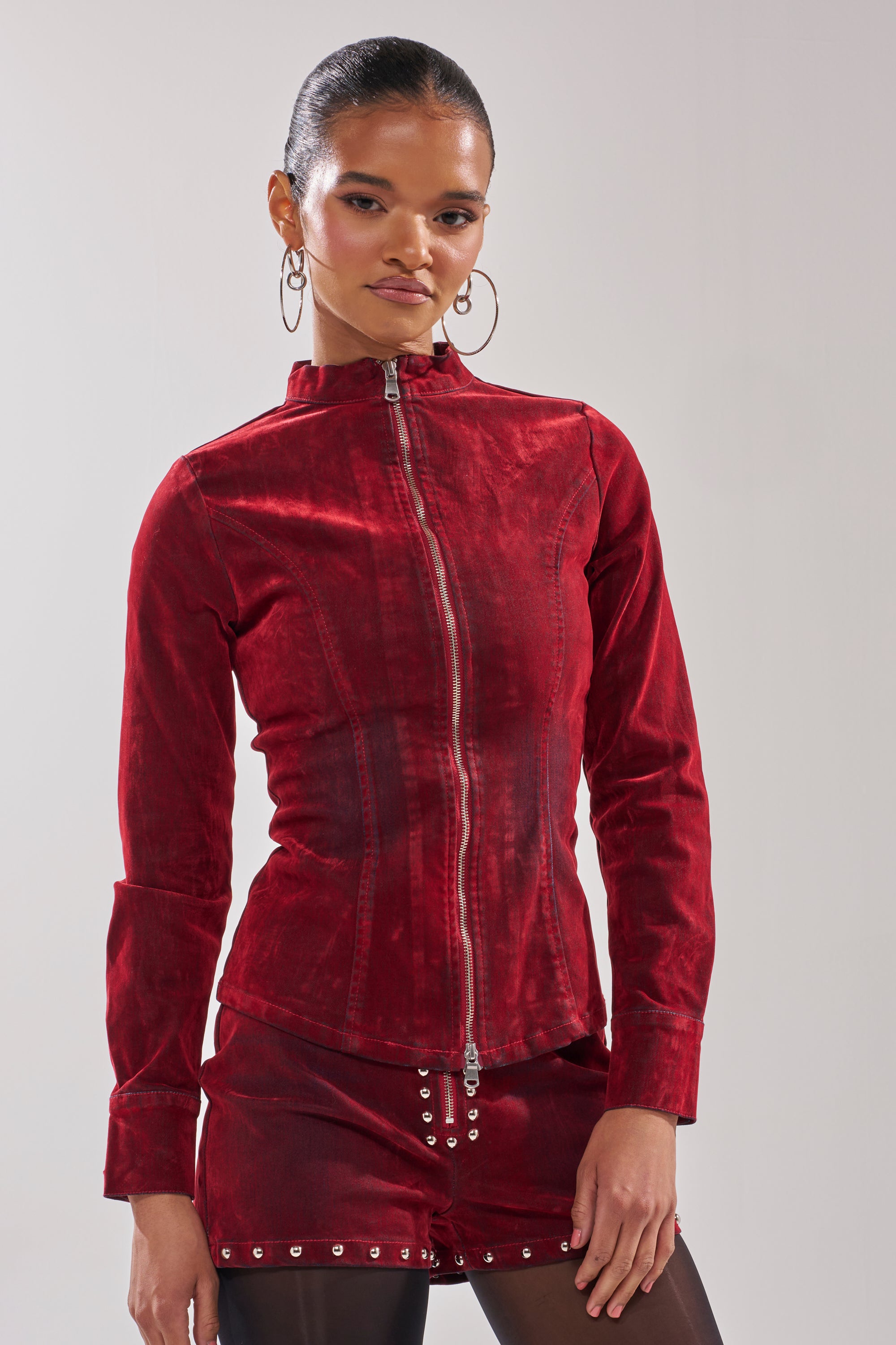 Against a plain background, a woman wears the RODEO VIBES VELVET DENIM ZIP UP with matching shorts, large hoop earrings, and black tights. The fitted long sleeves and tailored fit of the jacket create a bold, cohesive look.