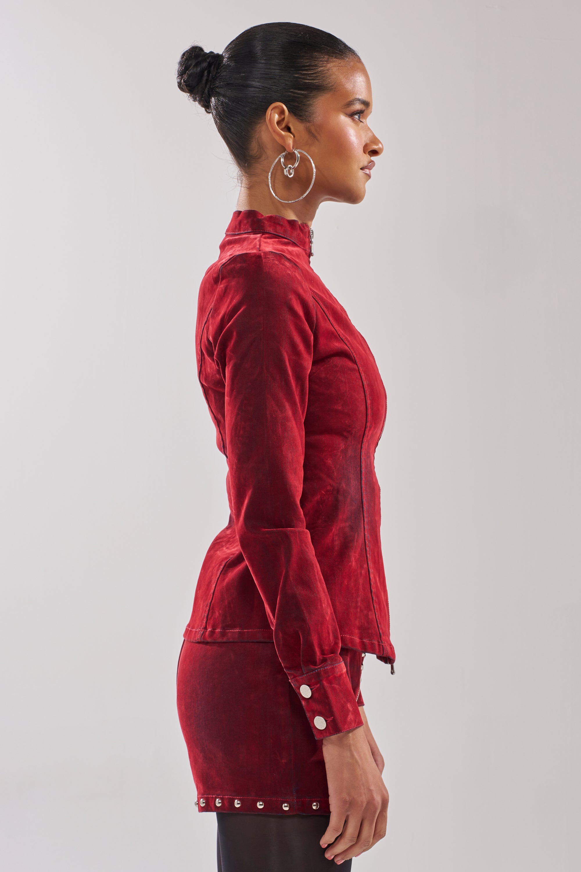 A woman with dark hair in a bun stands in profile against a plain background, wearing the RODEO VIBES VELVET DENIM ZIP UP and large hoop earrings.
