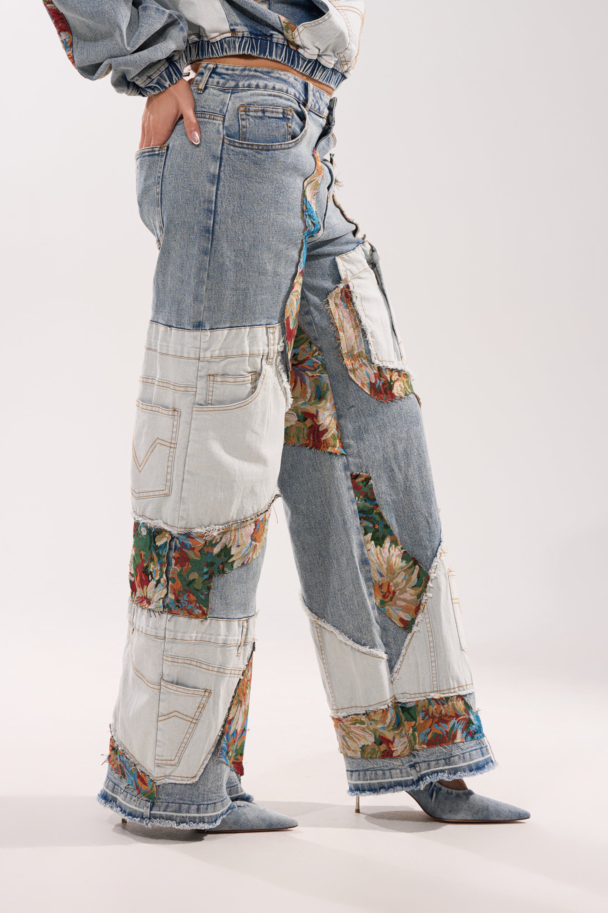 A person wearing the CHANGE IT UP WIDE LEG DENIM featuring floral and mixed-wash patchwork, visible stitching, and a vintage vibe, paired with pointed-toe denim heels in light and medium blue shades.