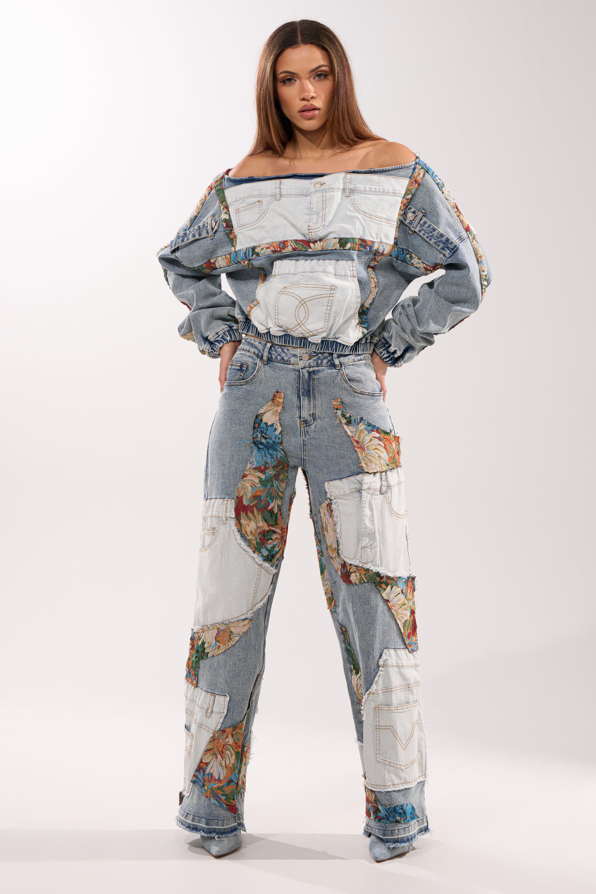 Woman standing against a plain background wearing the CHANGE IT UP WIDE LEG DENIM—patchwork wide-leg jeans with a high-rise waist, featuring floral and light mixed-wash denim fabric accents, paired with an off-the-shoulder denim top.