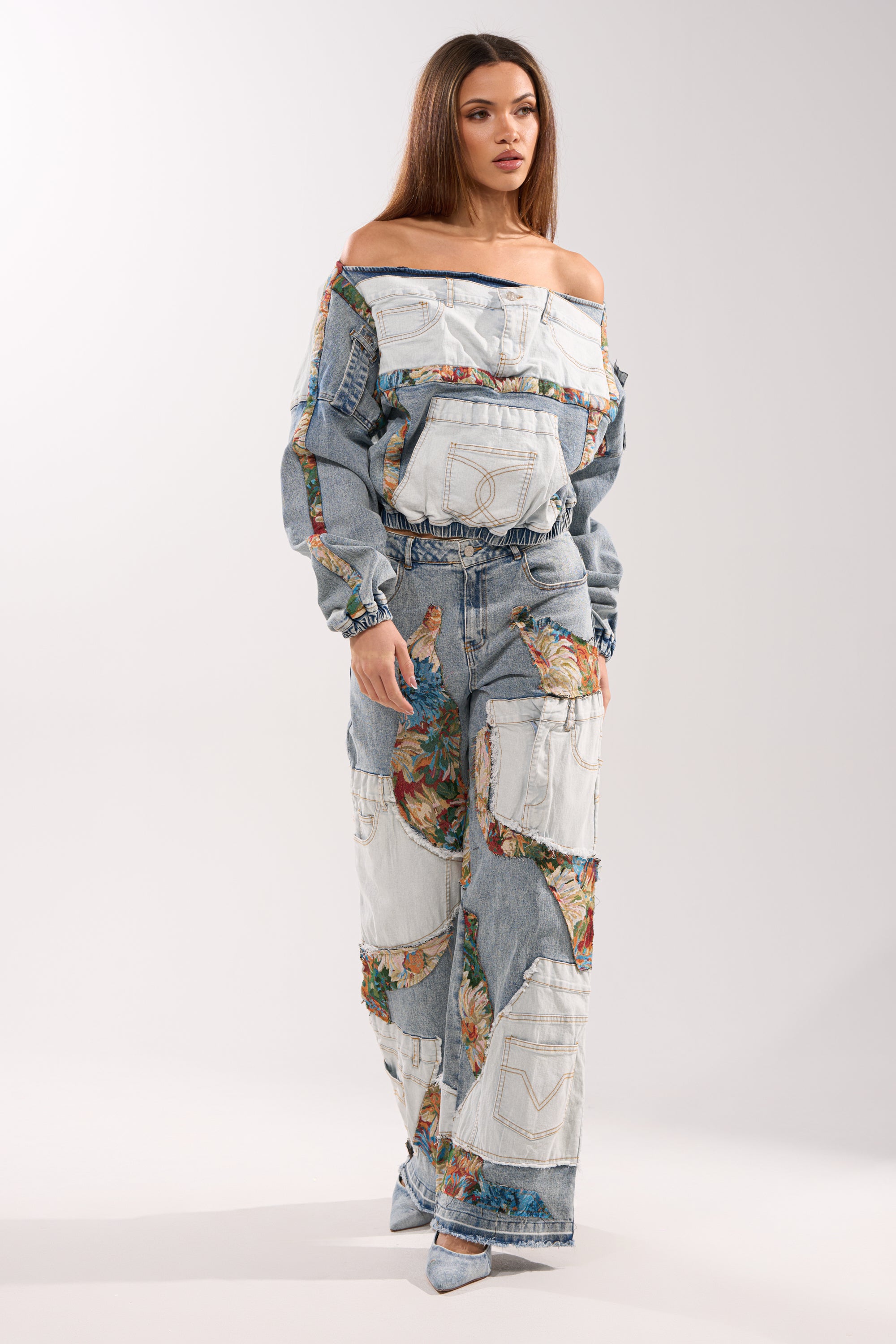 A woman wears the CHANGE IT UP DENIM SWEATSHIRT featuring patchwork denim and floral accents, styled street-style with wide-leg pants, denim pockets, and pointed-toe shoes.