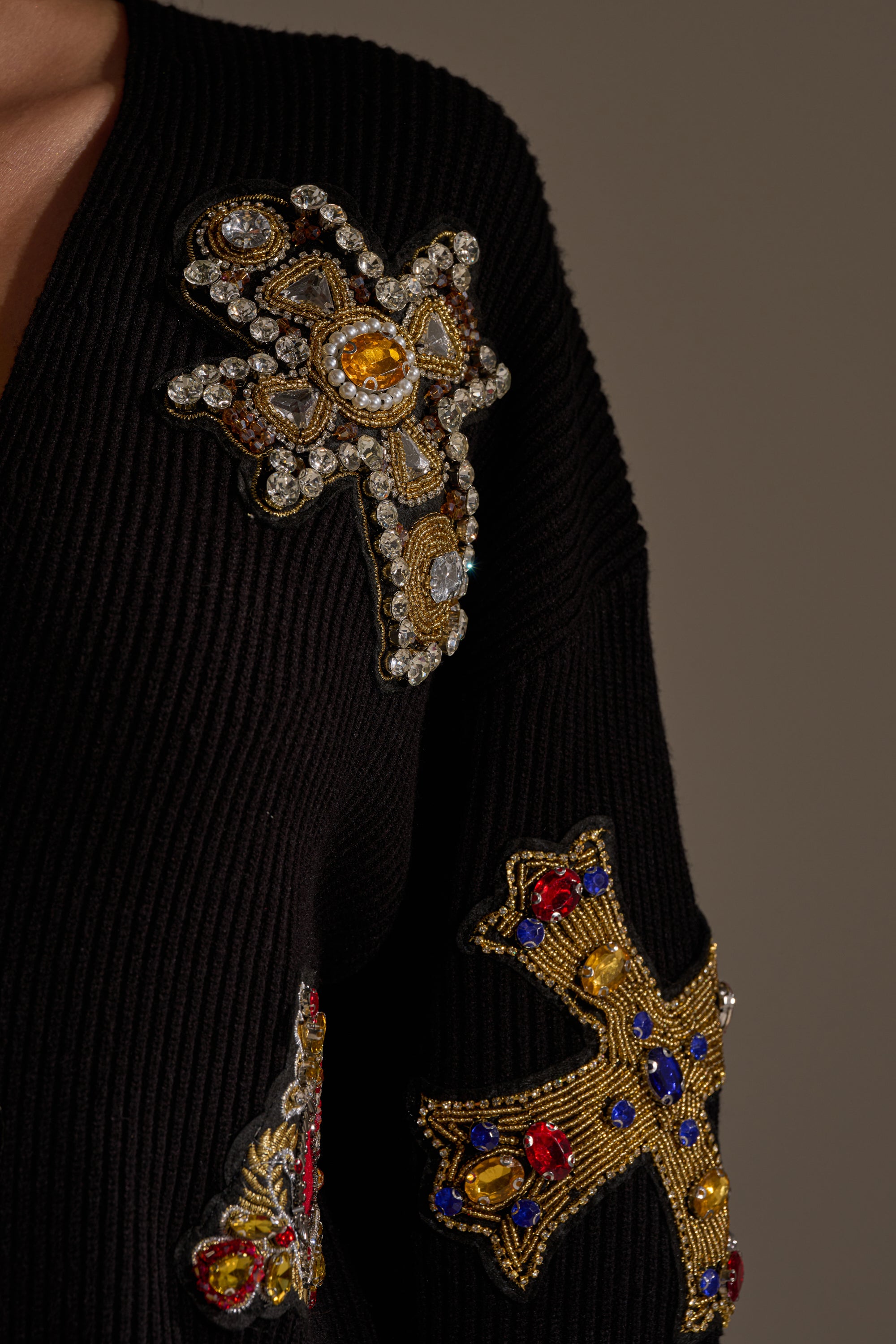 The FEELING EXTRA EMBELLISHED SWEATER features gold, red, and blue jeweled cross-shaped designs with rhinestones and intricate embroidery on a chic black oversized silhouette. 10