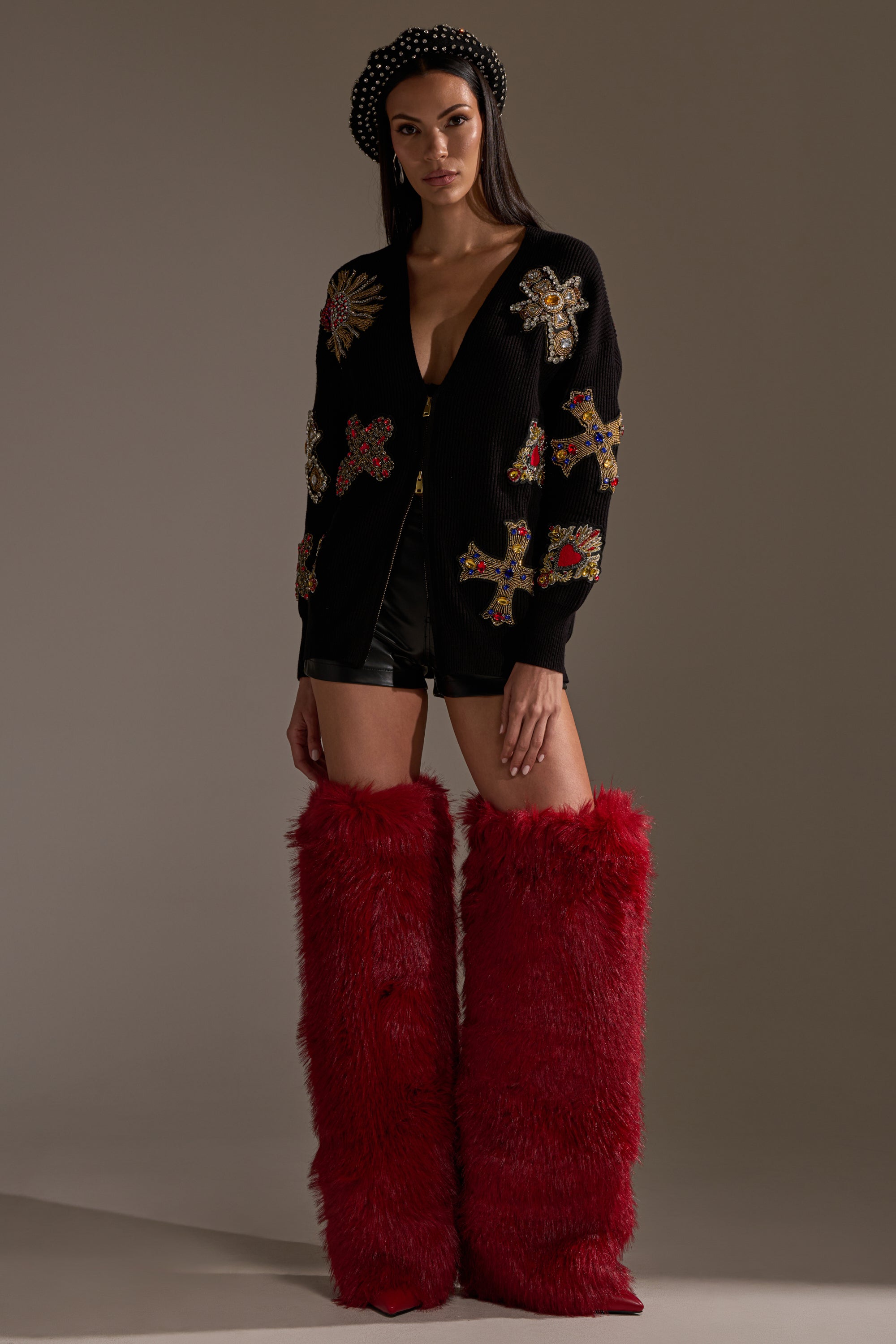 A woman in the FEELING EXTRA EMBELLISHED SWEATER, styled with black shorts and tall, fuzzy red boots, stands confidently against a plain background in an oversized silhouette. 8