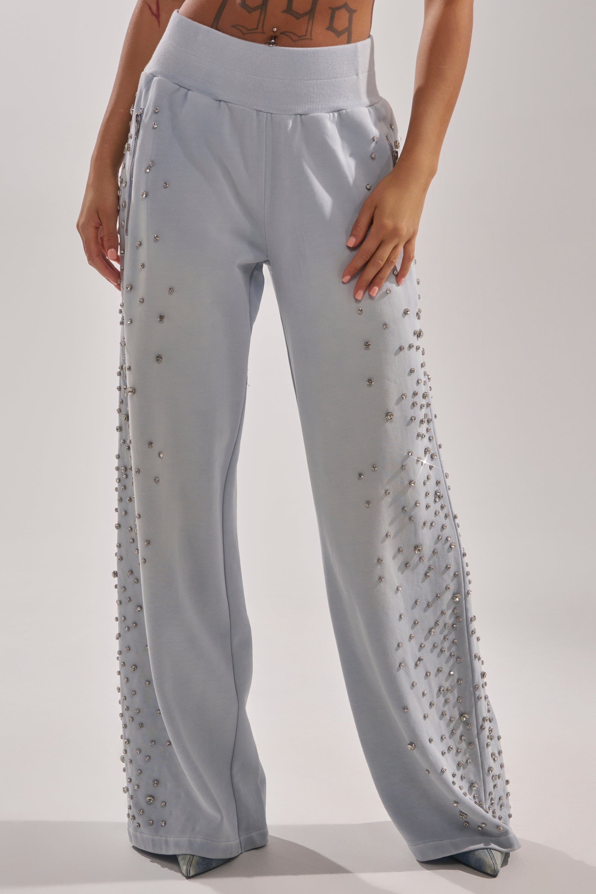 A person wears the OH HOT DAMN EMBELLISHED JOGGER in light blue, featuring pearl-like details along the sides; only their lower torso and legs are visible against a plain background. 1
