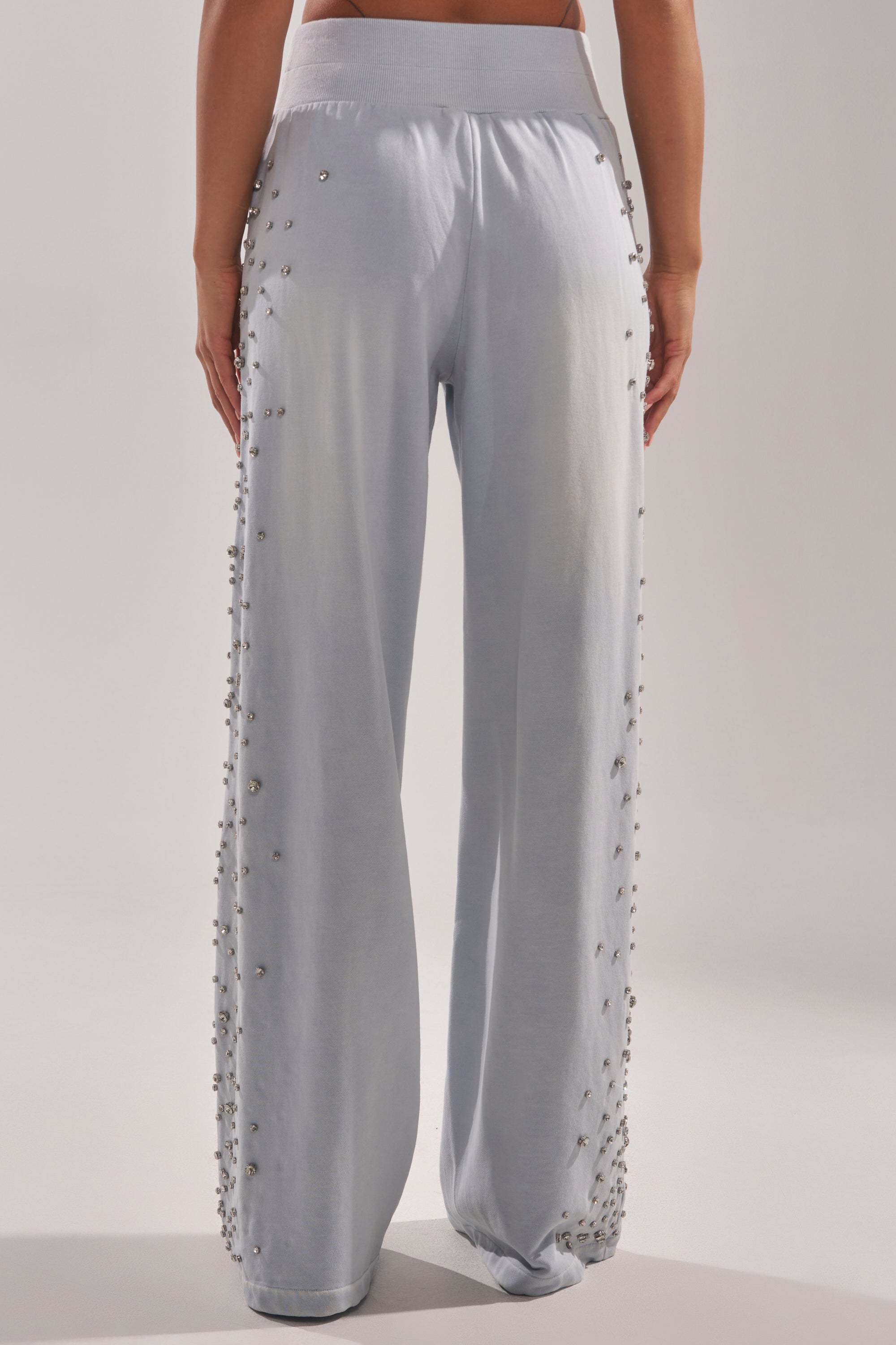 A person is seen from the back wearing the OH HOT DAMN EMBELLISHED JOGGER in light blue, featuring wide legs and small side embellishments. The pants look soft and comfortable, with the wearer’s bare lower back visible. 5