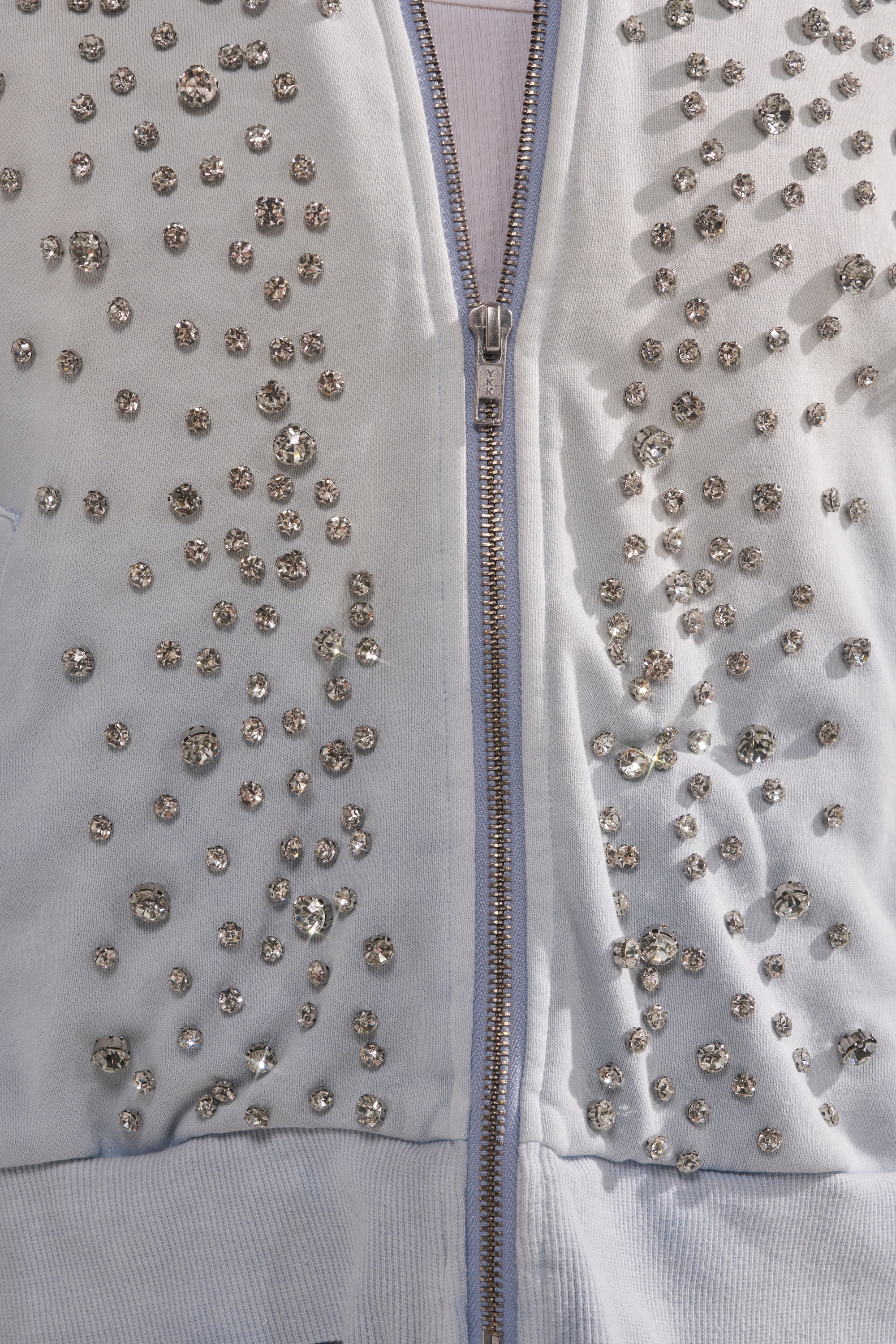 The OH HOT DAMN EMBELLISHED ZIP UP SWEATSHIRT is a light blue zip up sweatshirt decorated with sparkling rhinestones scattered across both sides of the zipper. 9