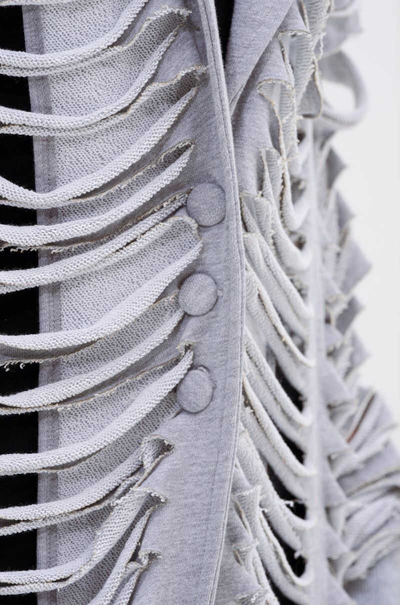 Close-up of the CUT IT OUT FRENCH TERRY TRENCH, featuring horizontal distressed fringed strips with three round fabric-covered buttons on the front and black visible through the cut-outs. 8