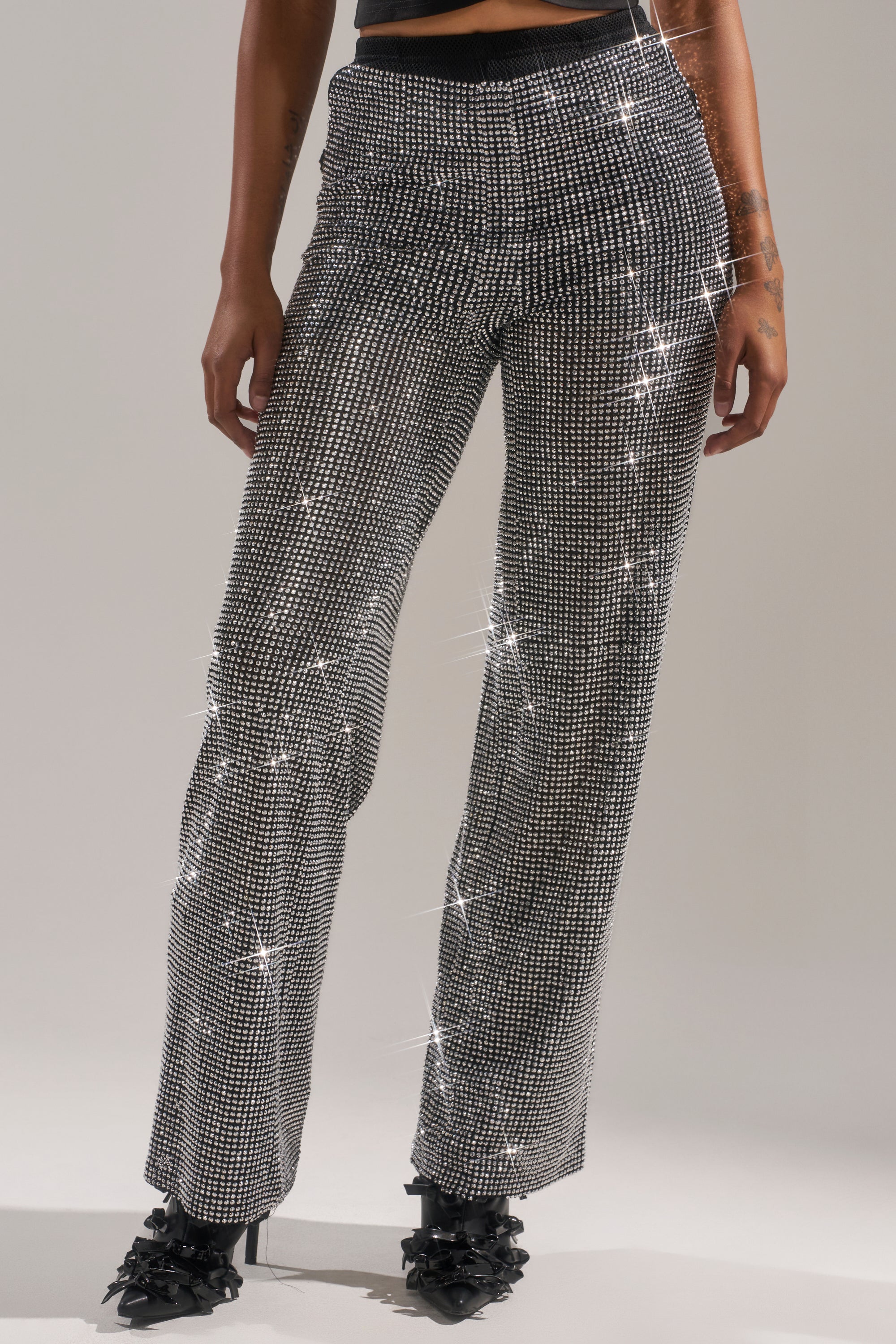 A person models the LET IT GO RHINESTONE WIDE LEG PANT with glitter and rhinestone detailing, paired with embellished black heels, against a plain background. Only the lower torso and legs are shown.